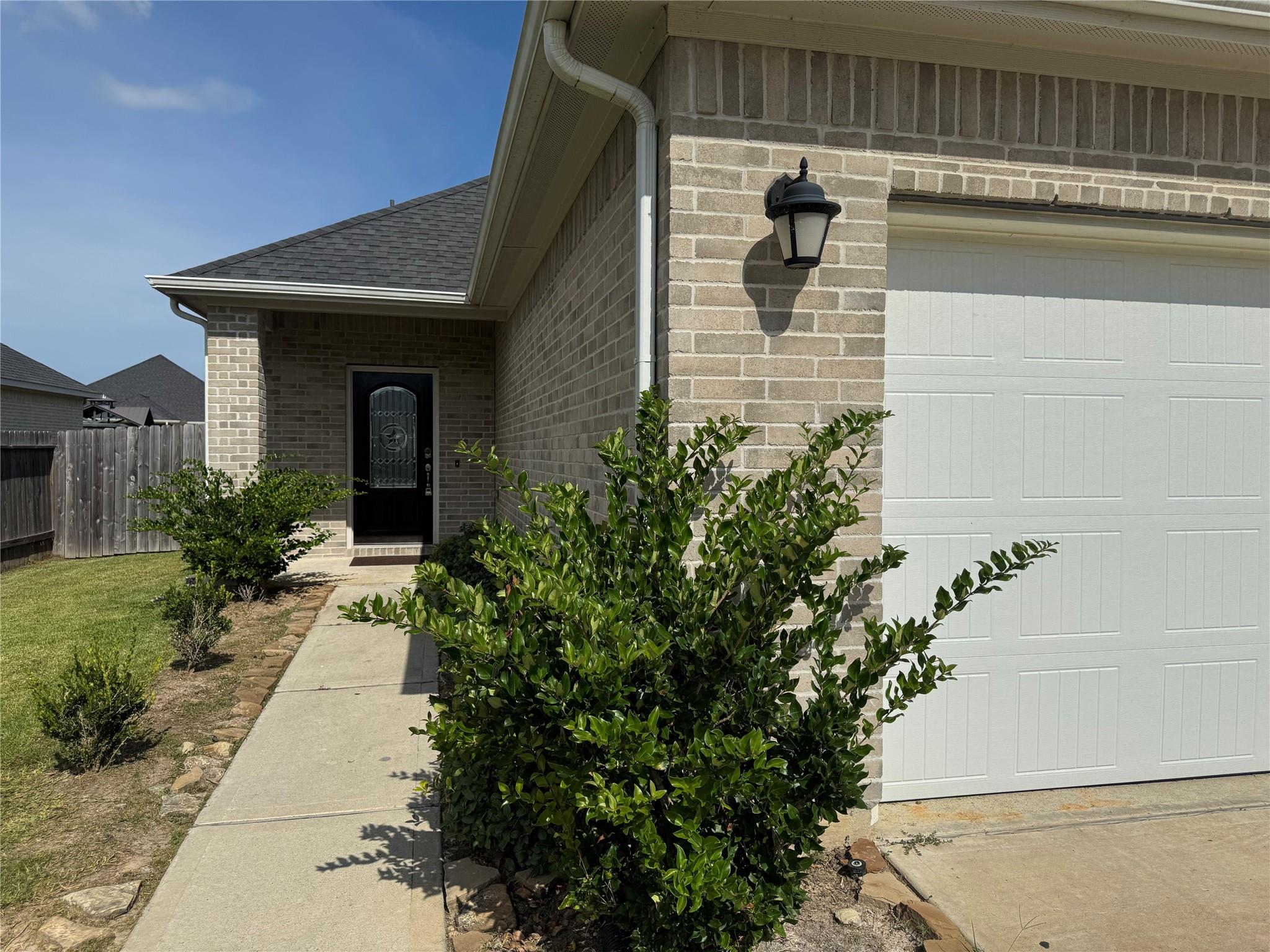Brick home exterior with a white garage door, recessed entry, and front shrubs.