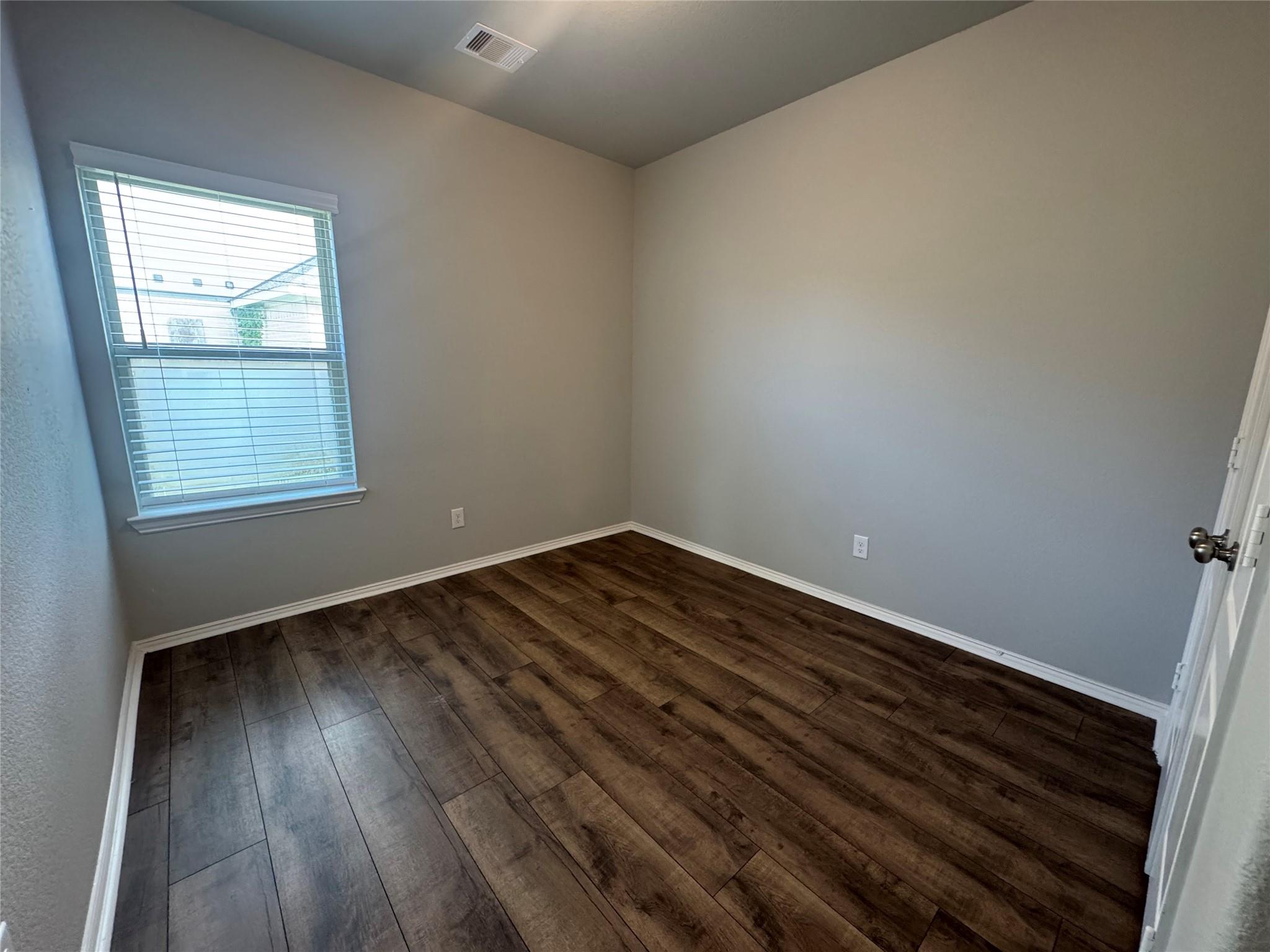 Empty room with dark wood-look flooring, gray walls, and a window with blinds.