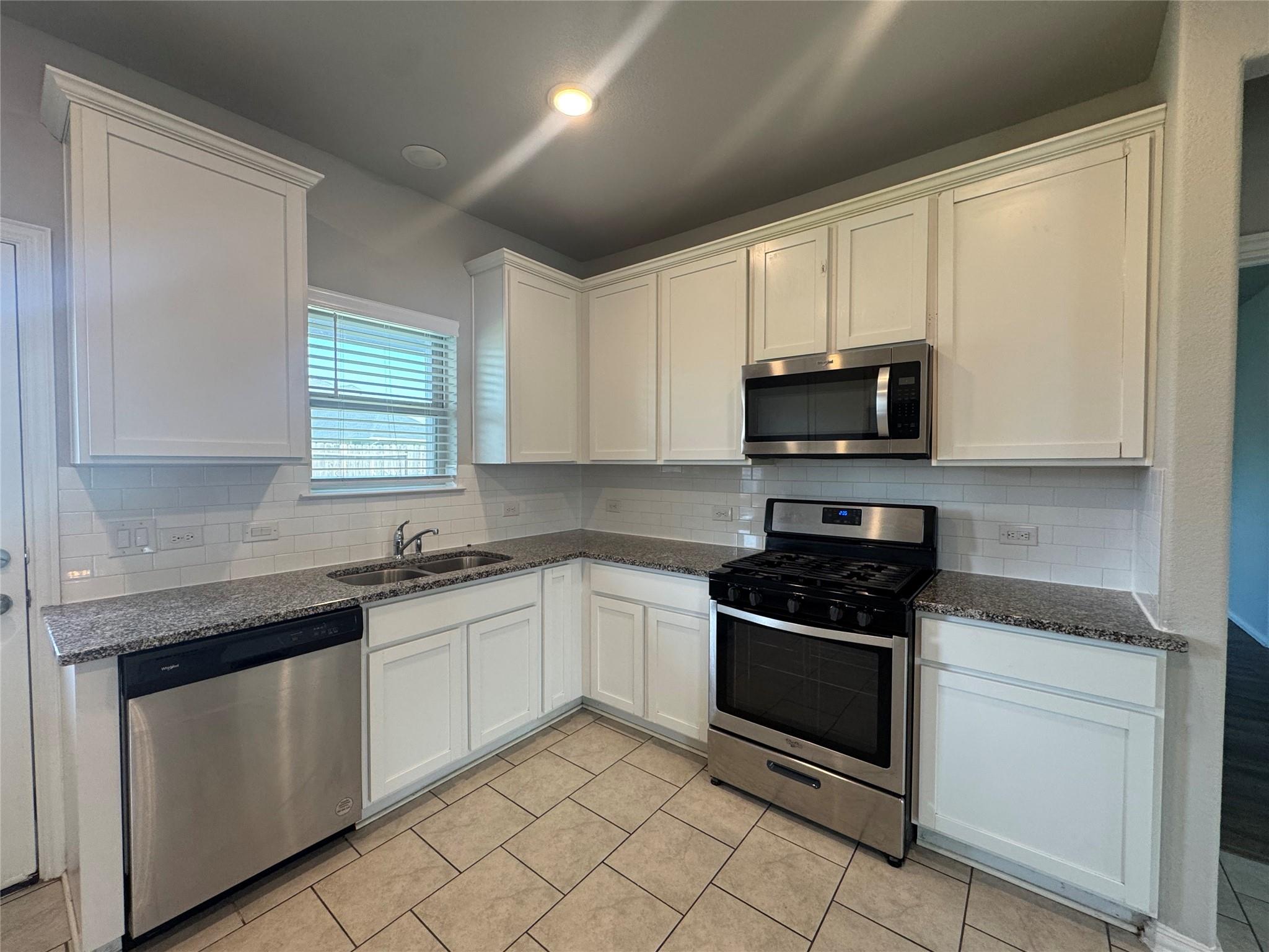 Kitchen with white cabinets, granite counters, stainless steel appliances, and tan tile flooring.
