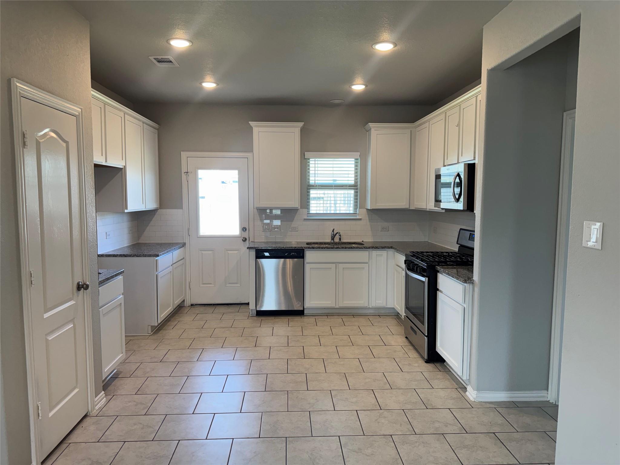Kitchen with white cabinets, granite countertops, tile floors, and stainless steel appliances.