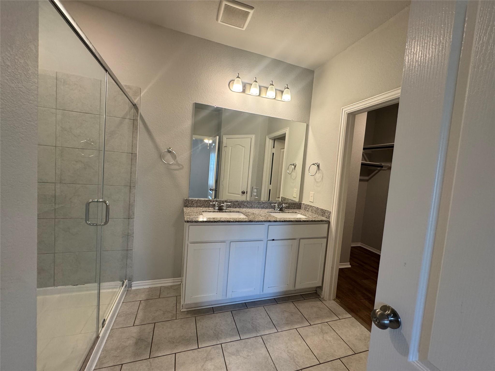 Bathroom with a glass shower and double-sink vanity topped with speckled granite.