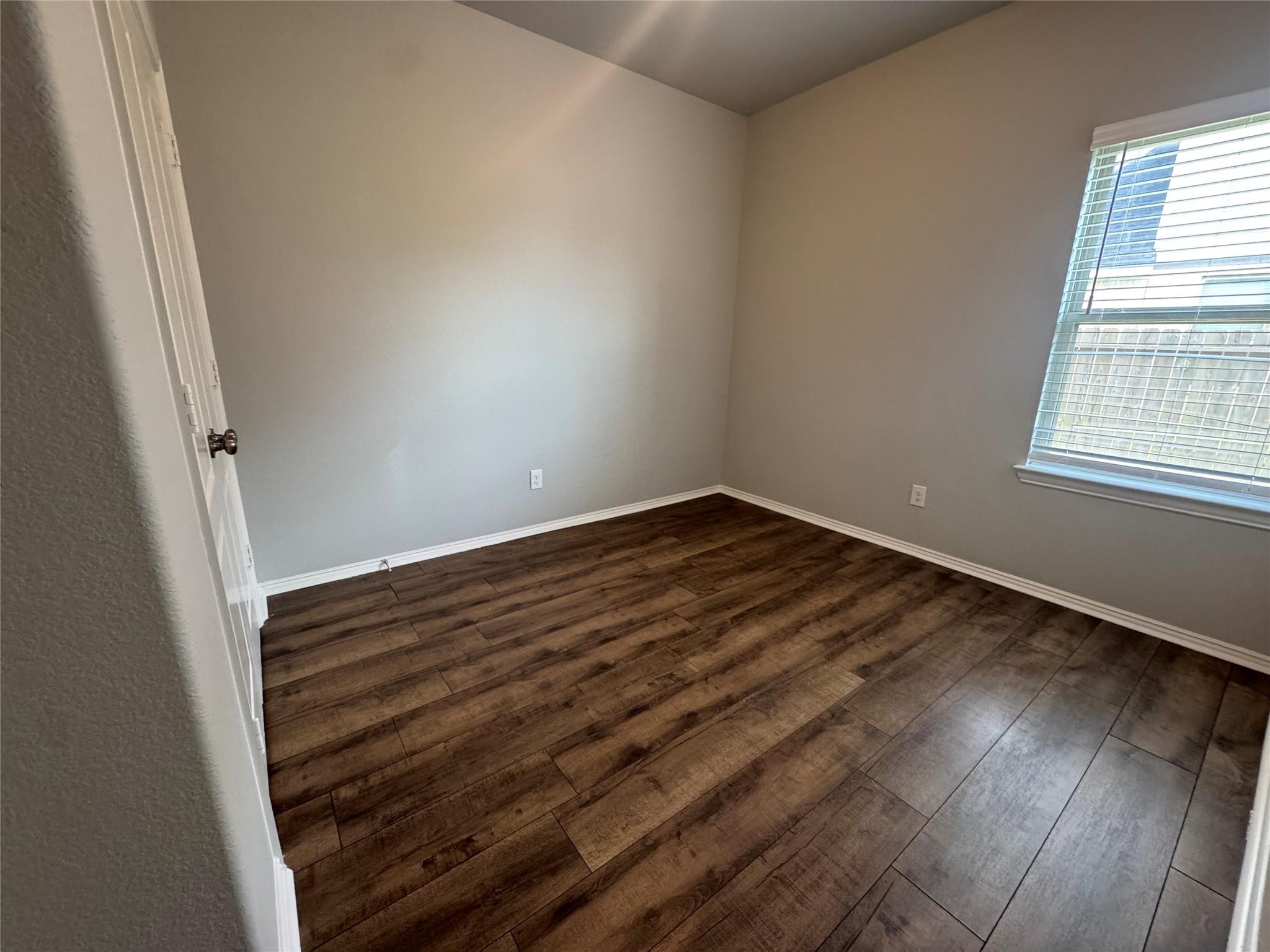 Empty room with dark plank flooring and a window with blinds.