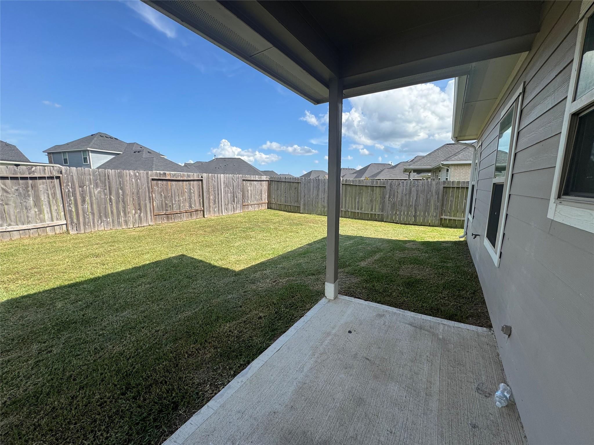 Covered patio overlooking a fenced grassy backyard, with neighboring homes beyond the fence.