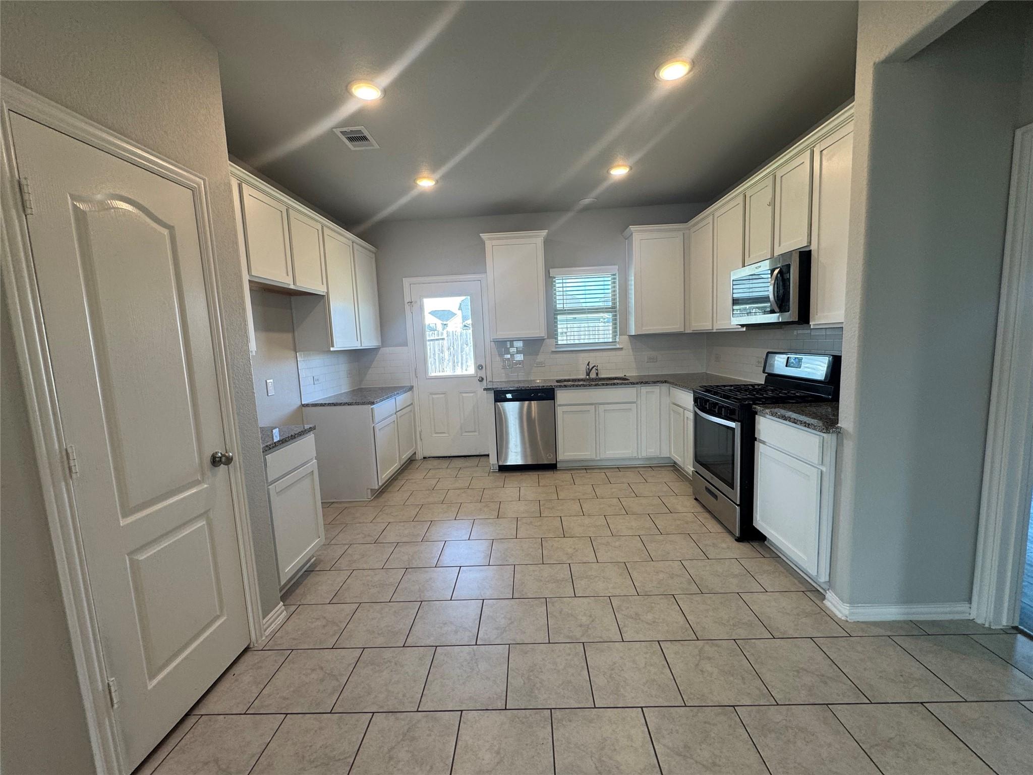 Kitchen with white cabinets, granite countertops, tile flooring, and stainless steel appliances.