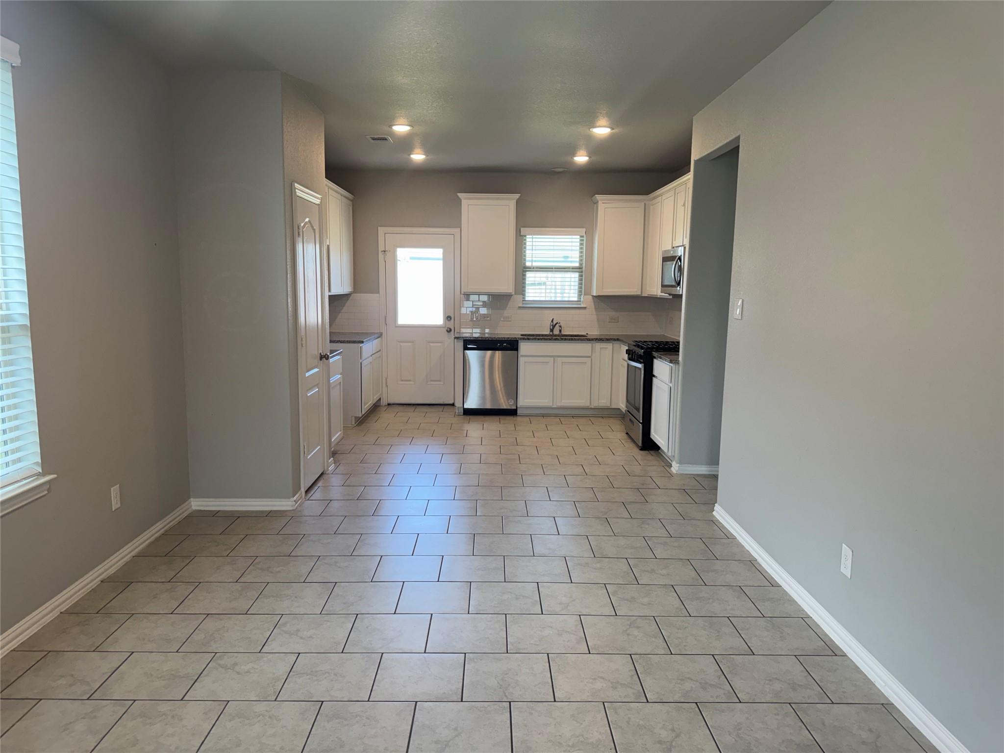 Unfurnished kitchen with white cabinets, stainless steel appliances, and a large tiled floor.