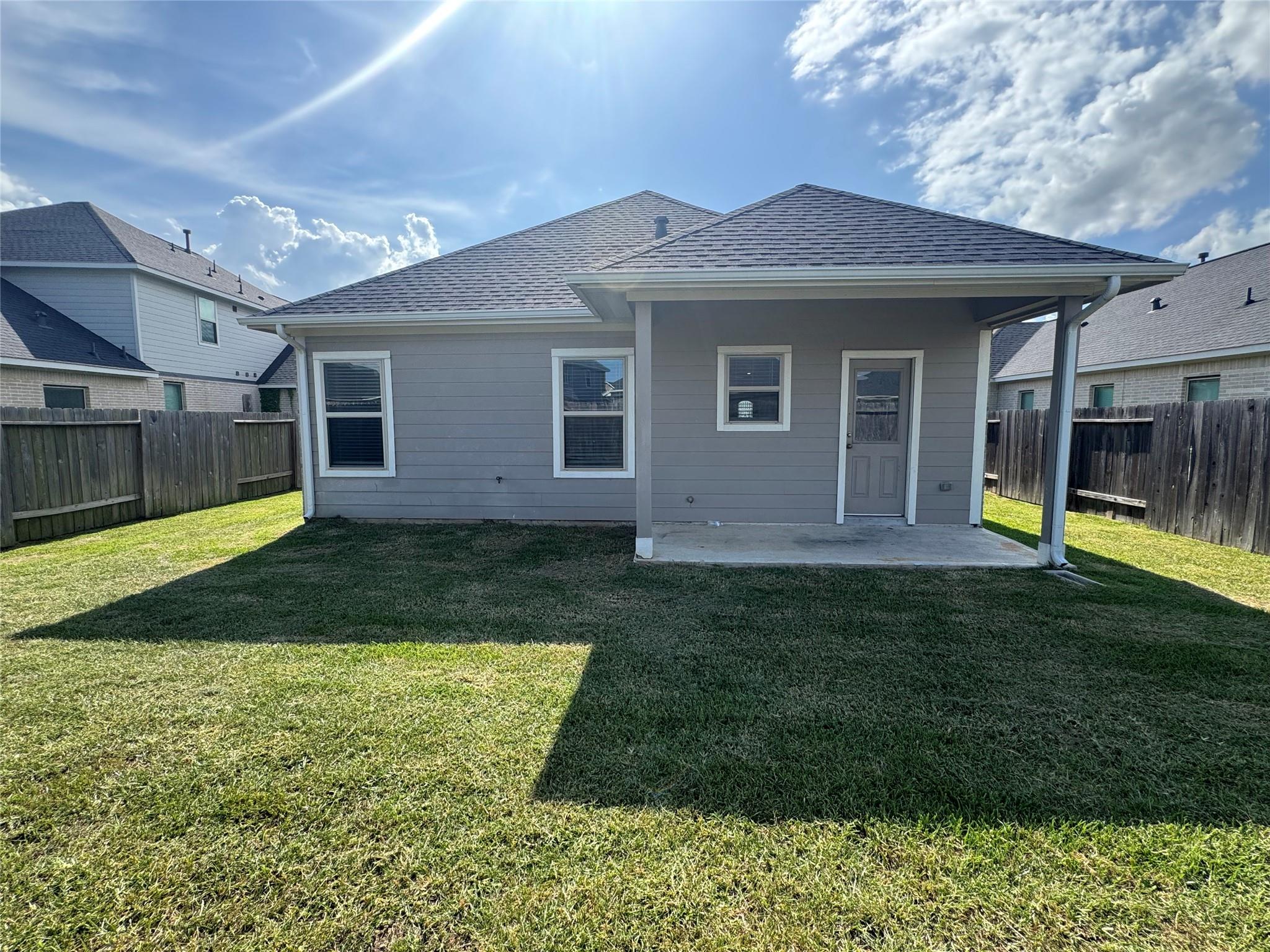 Rear of a gray-sided home with a covered patio and fenced grassy yard.