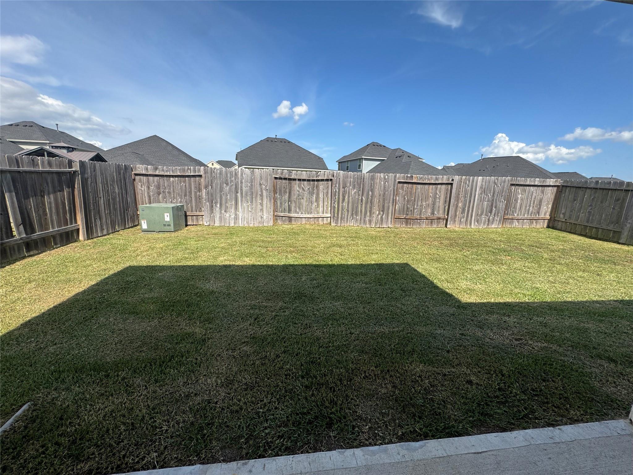 Fenced backyard with a broad grassy lawn, weathered wooden privacy fence, and neighboring rooftops.