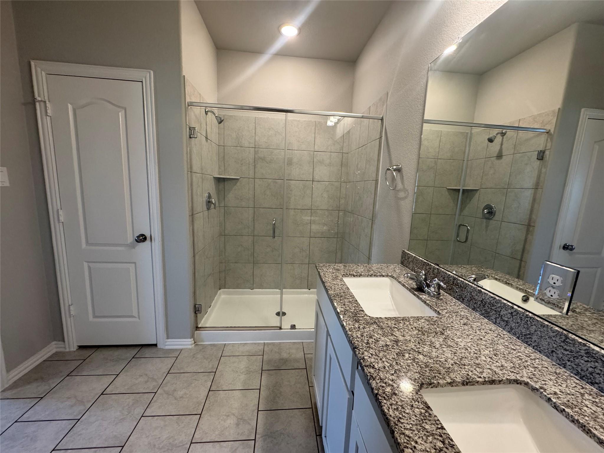 Bathroom with a glass-enclosed tiled shower and double-sink granite vanity.