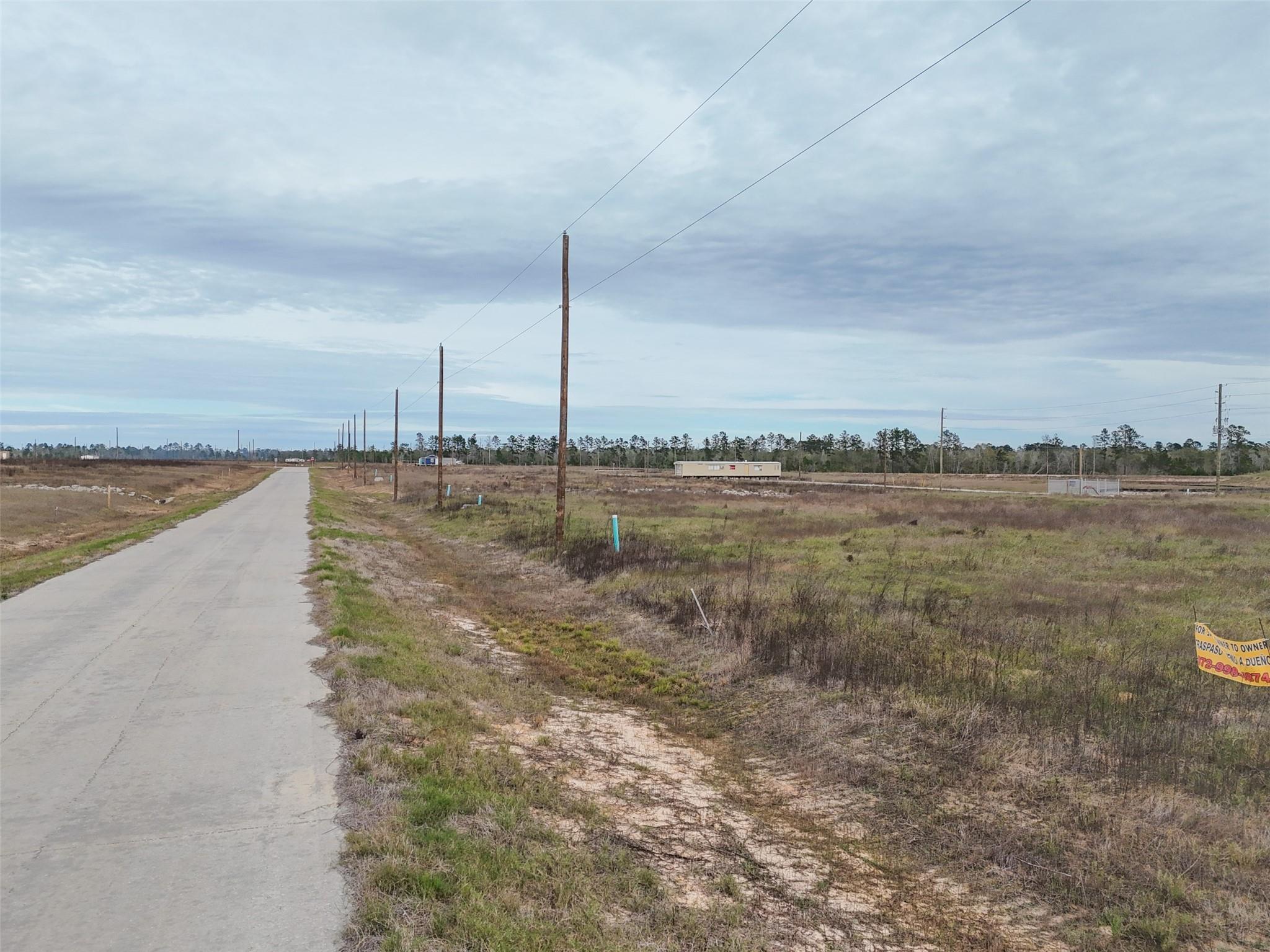 Vacant grassy parcel beside a paved road, with utility poles and a partly visible no-trespassing sign.