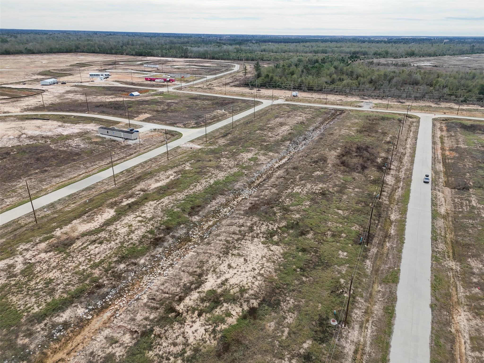 Aerial view of vacant lots crossed by paved roads and a rocky drainage channel.