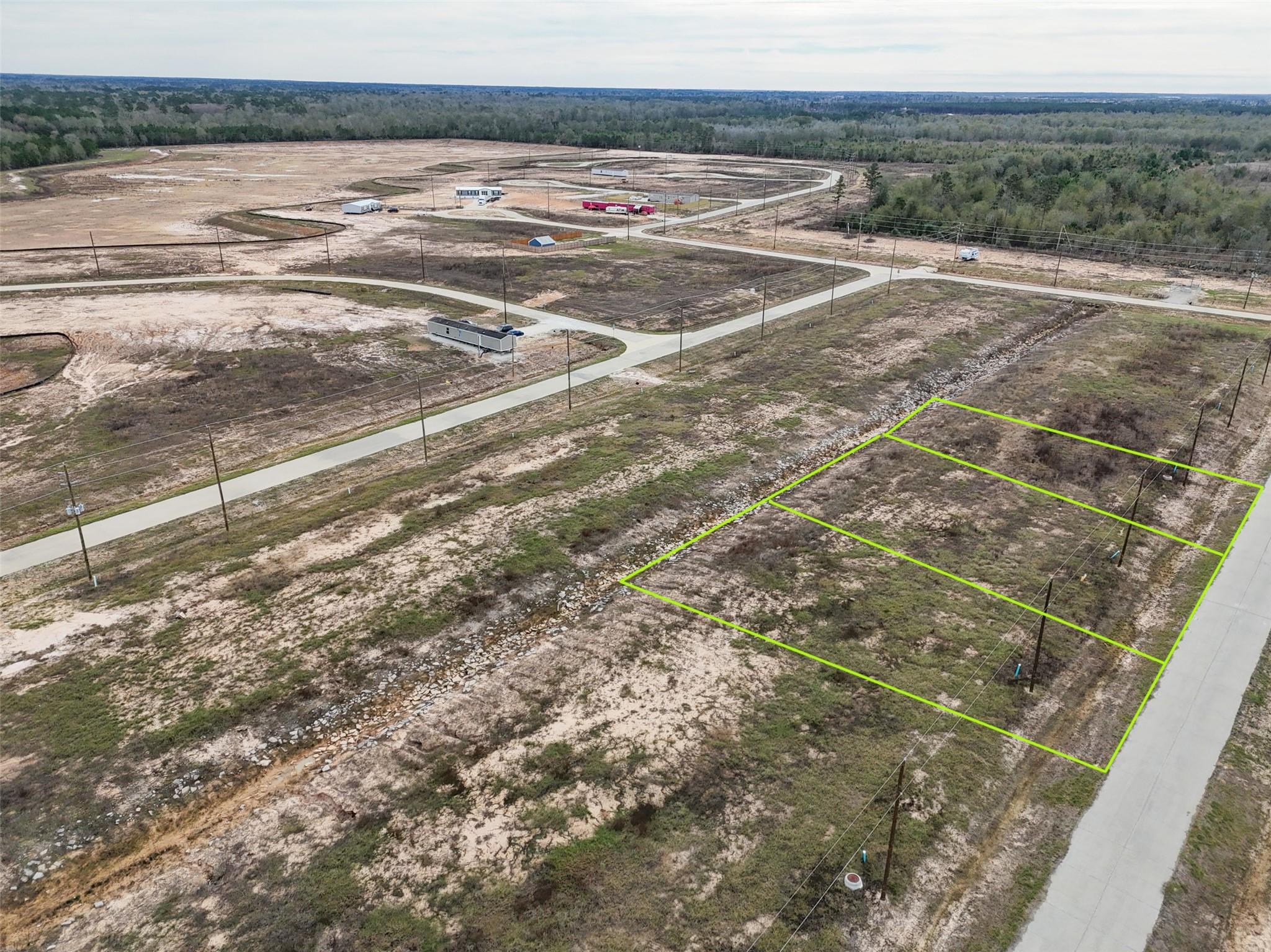 Vacant lot outlined in green beside a paved road, with cleared parcels and woods beyond.