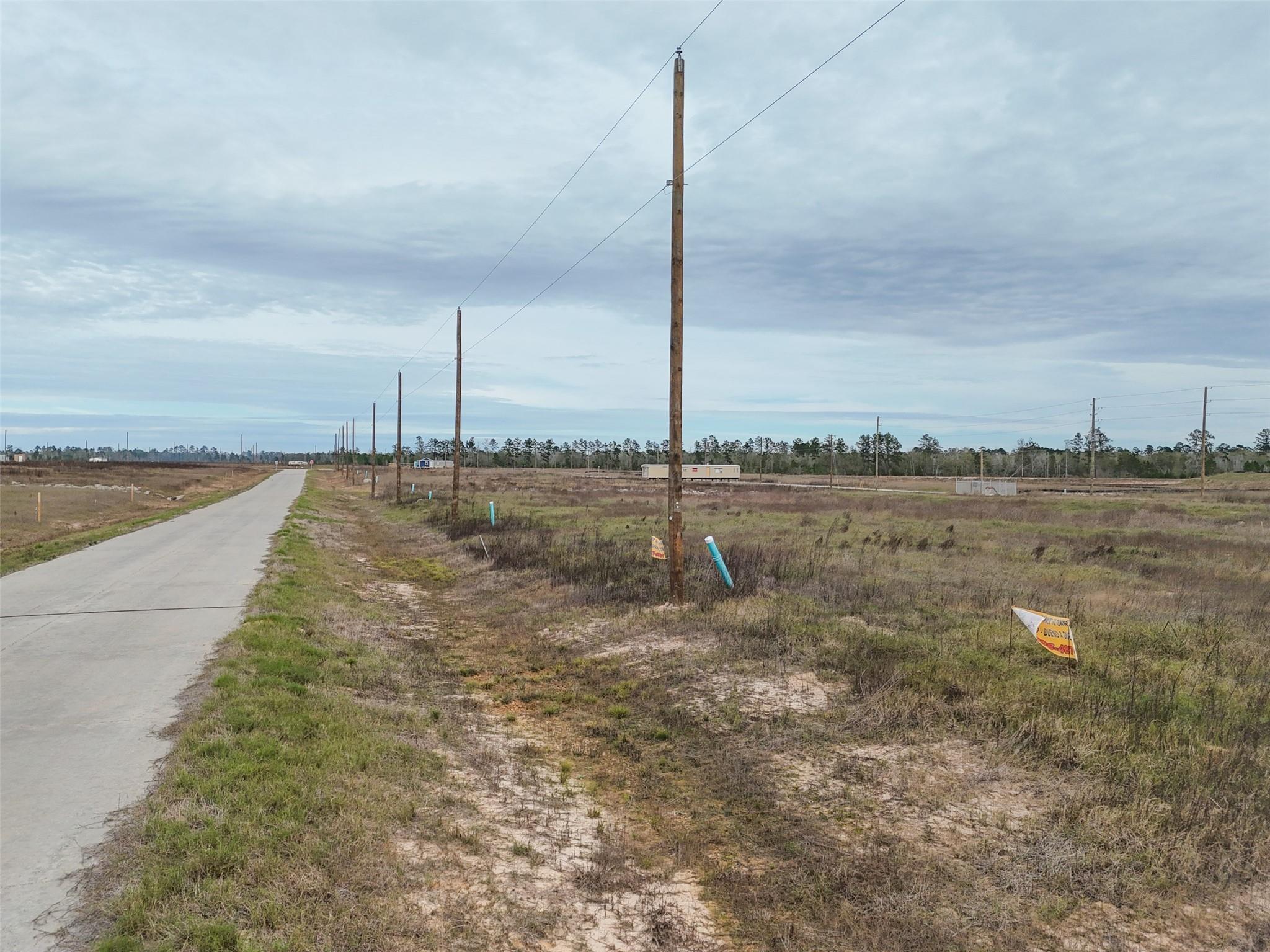 Vacant grassy lot beside a paved road, with utility poles and overhead wires.
