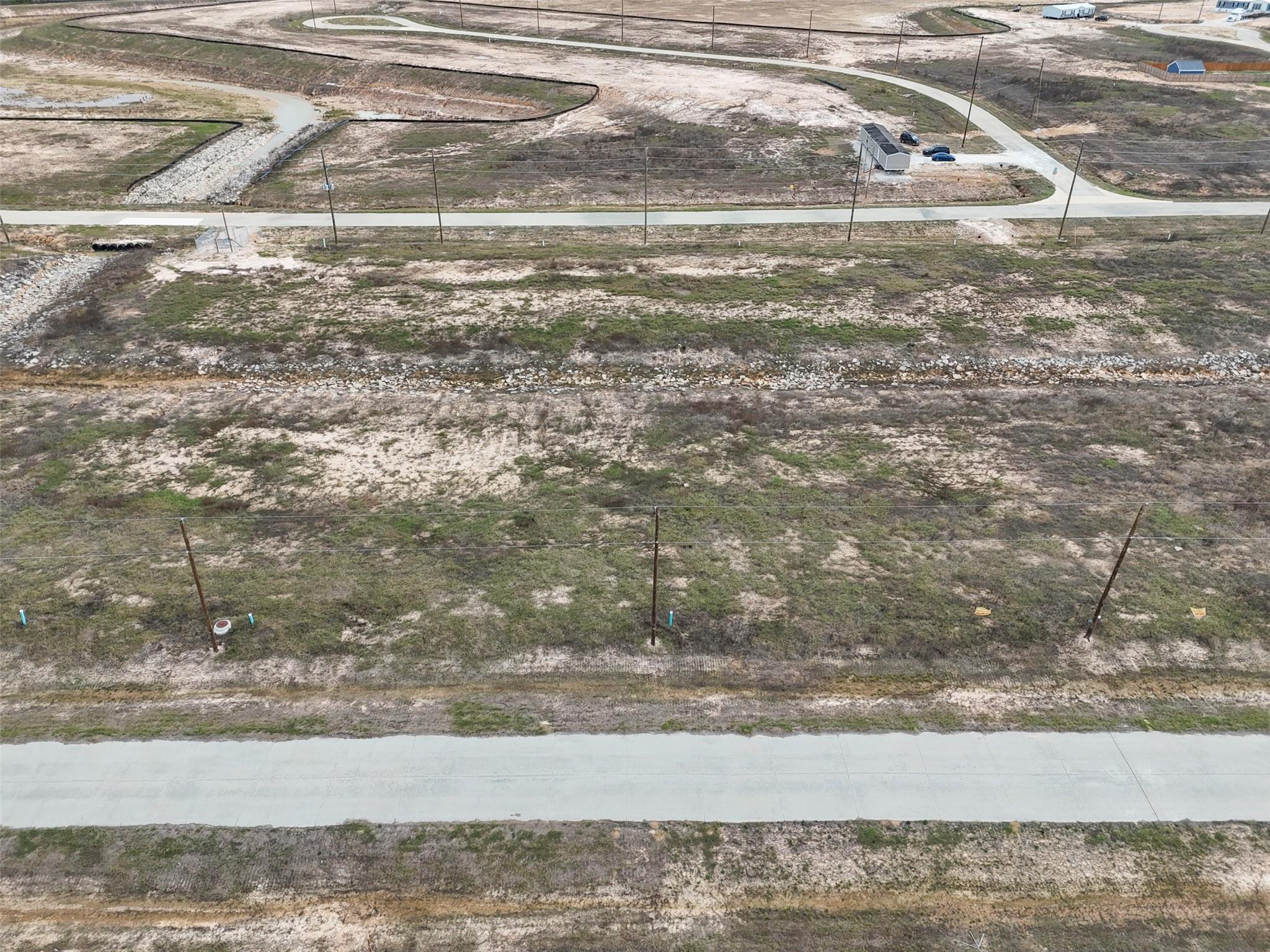 Aerial view of a vacant lot beside a concrete sidewalk, with a wire fence and subdivision roads nearby.