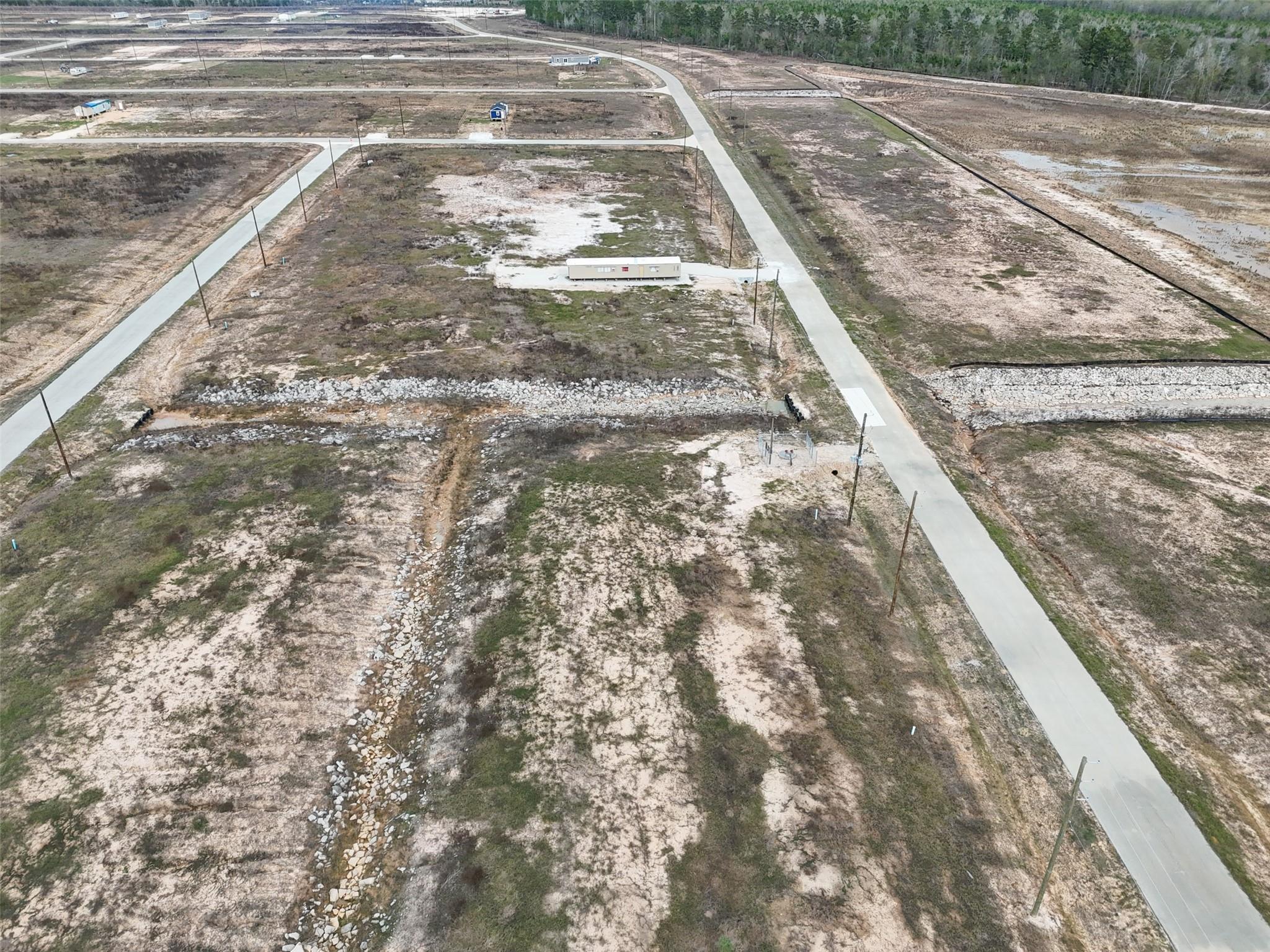 Aerial view of sandy subdivision lots with paved roads and rocky drainage channels.