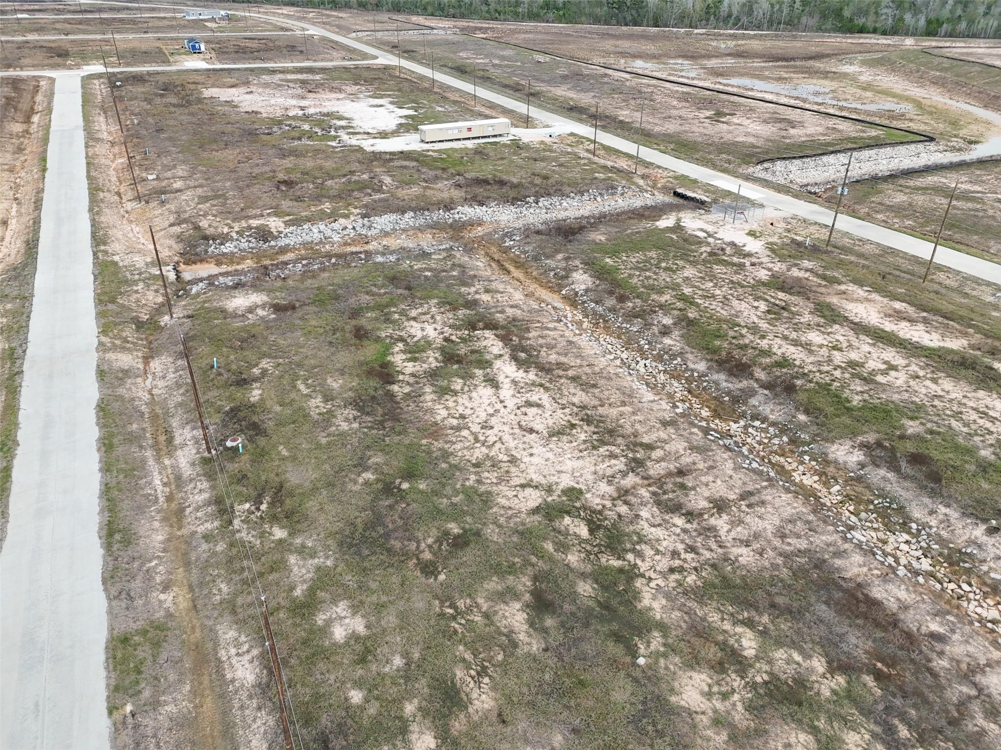 Undeveloped lot with rock-lined drainage channels beside paved subdivision roads.