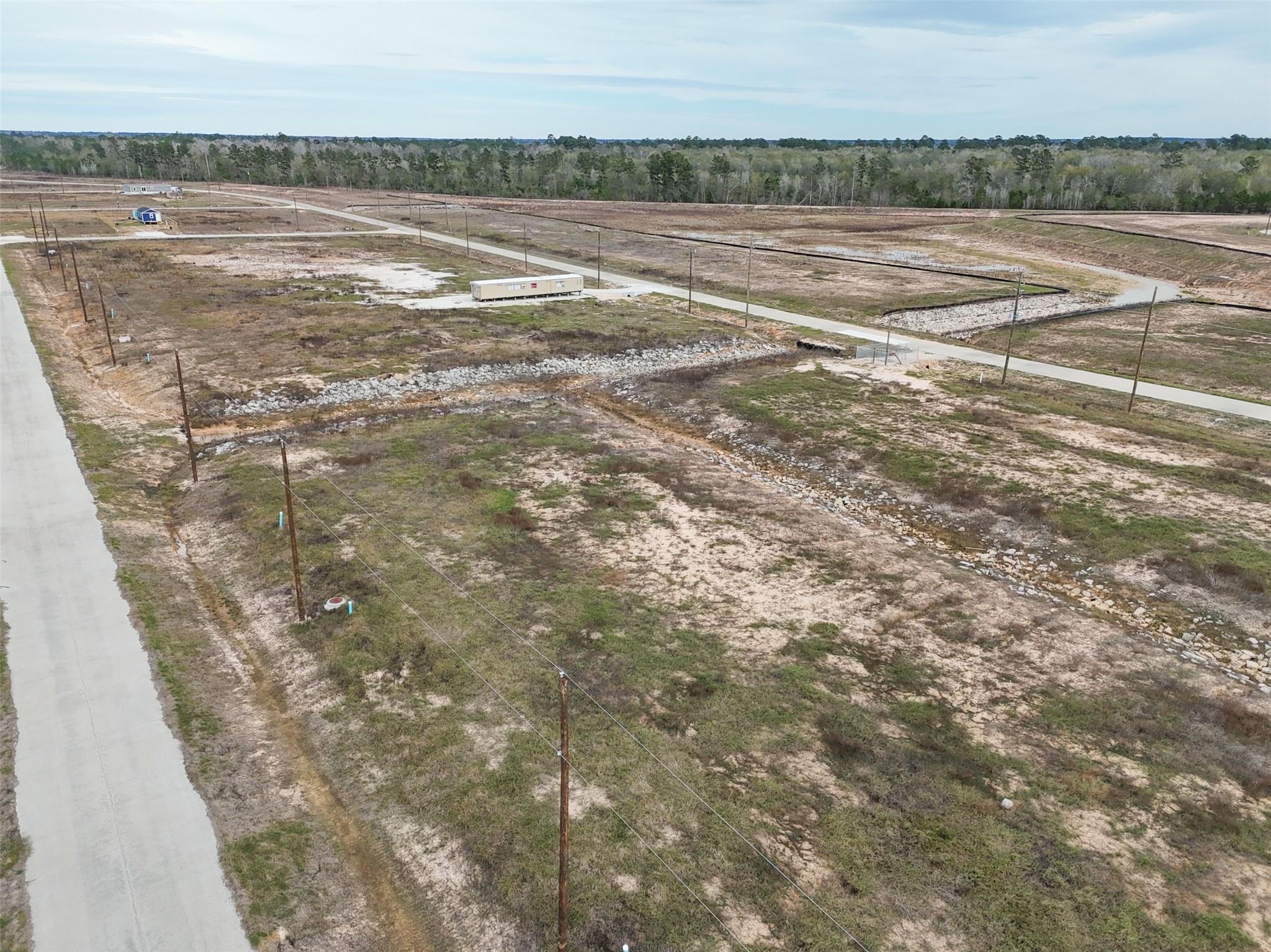 Aerial view of undeveloped sandy lots with new roads, utility poles, and drainage swales.