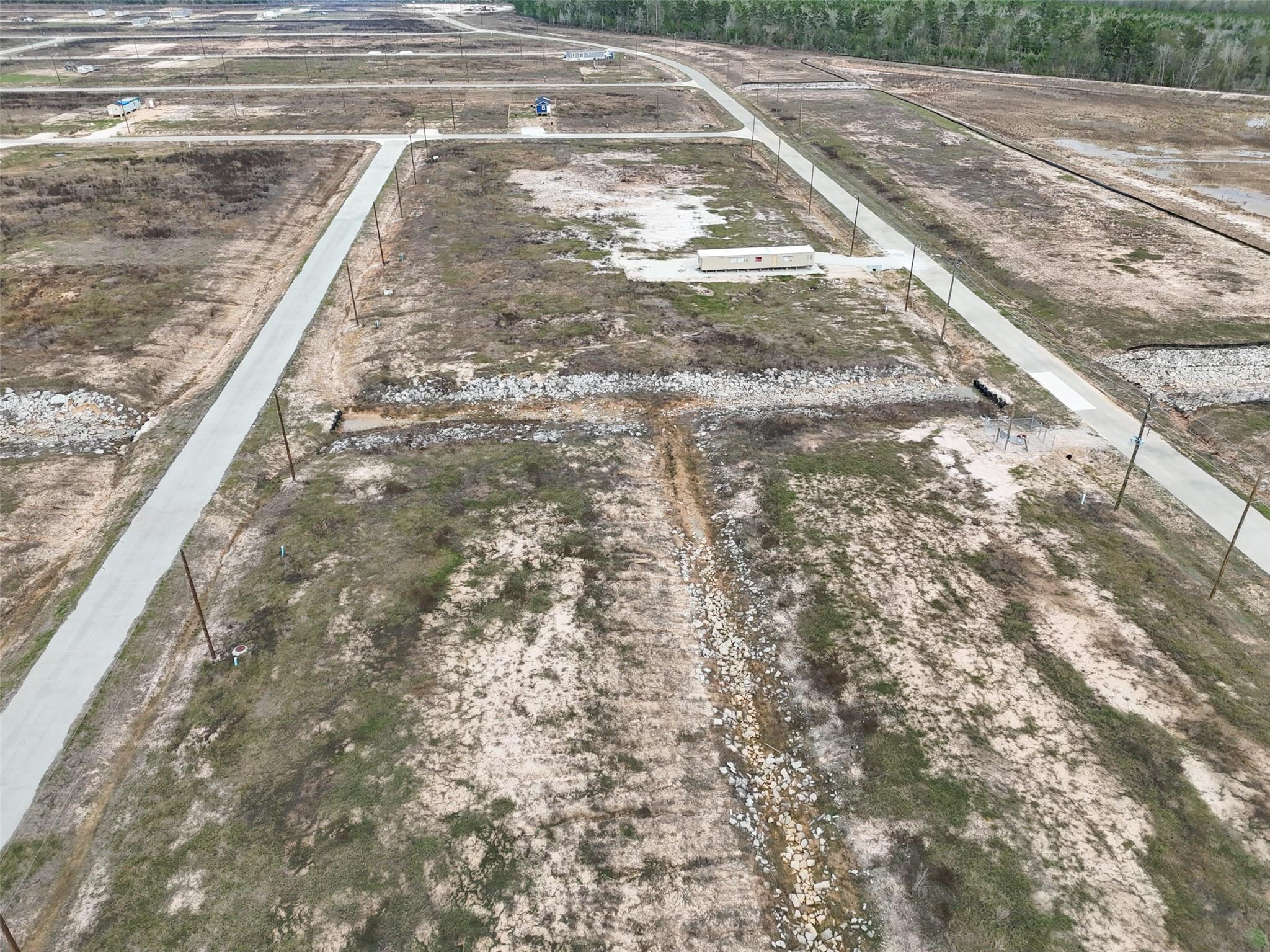 Aerial view of a vacant subdivision parcel with a rock-lined drainage channel and paved roads.