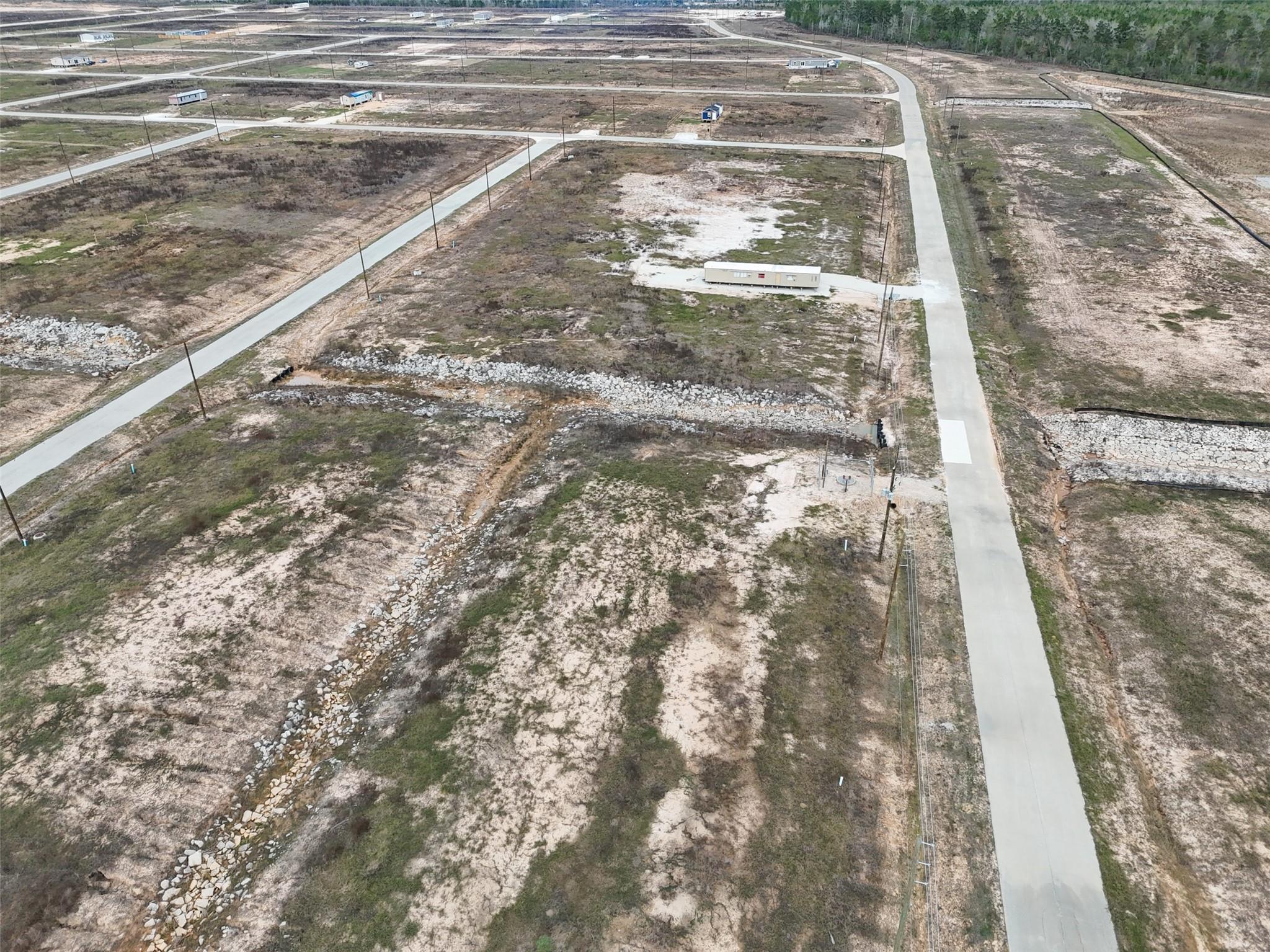 Aerial view of cleared subdivision lots with paved roads and a rock-lined drainage channel.