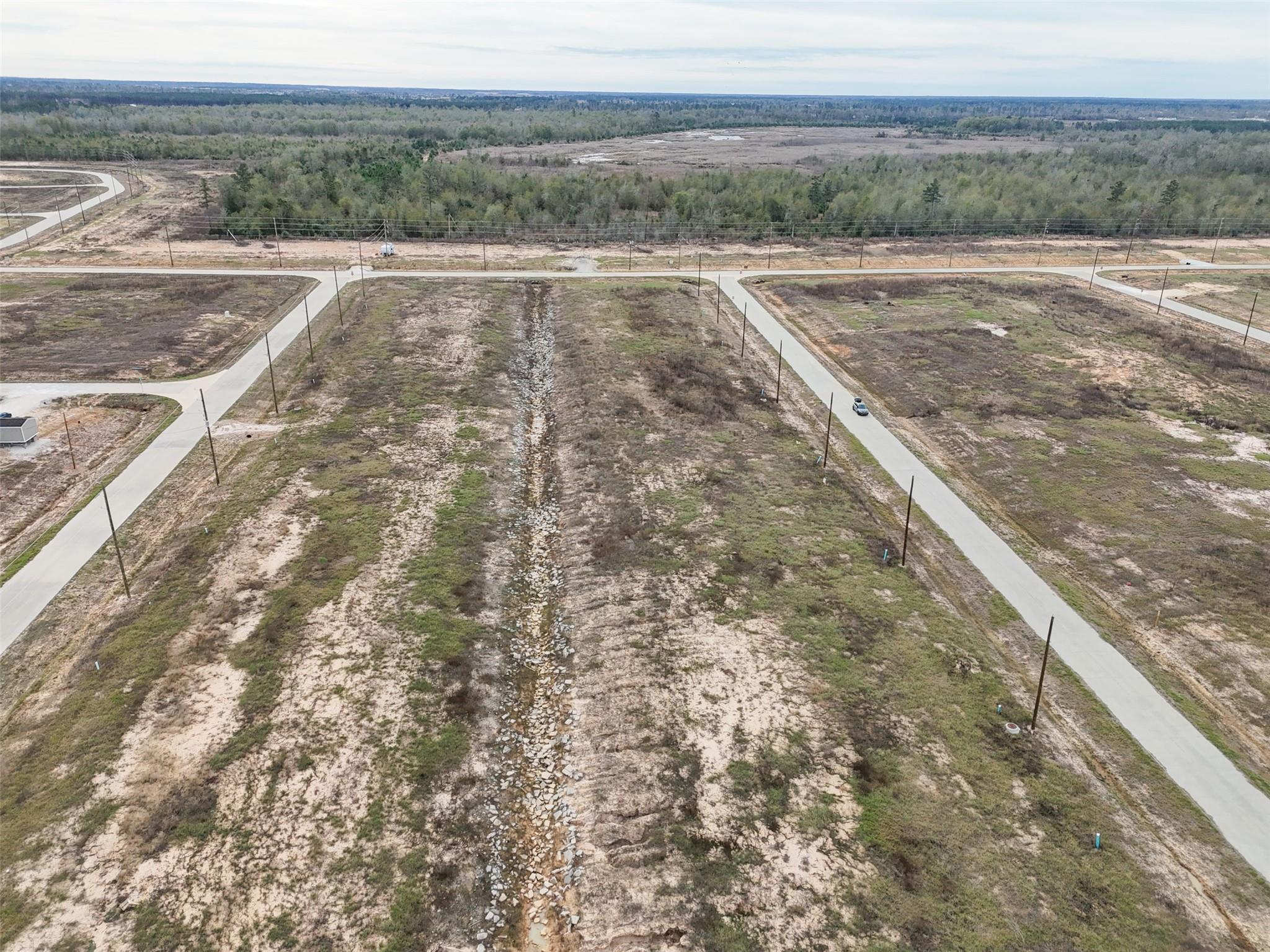 Aerial view of vacant scrubland lots divided by concrete roads, with a rocky drainage swale.