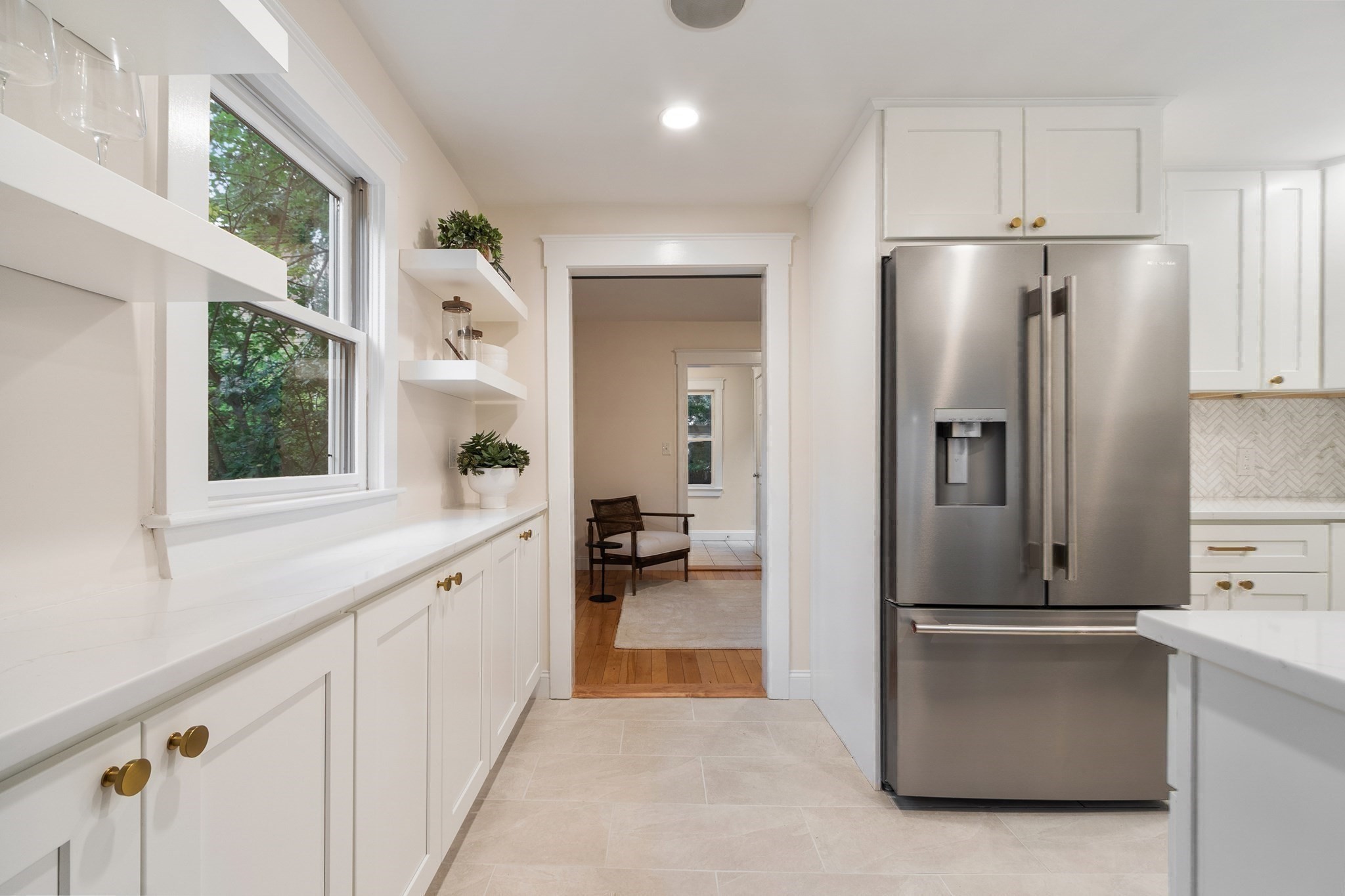 Bright white kitchen with open shelves, a large window, and a stainless steel French-door refrigerator.