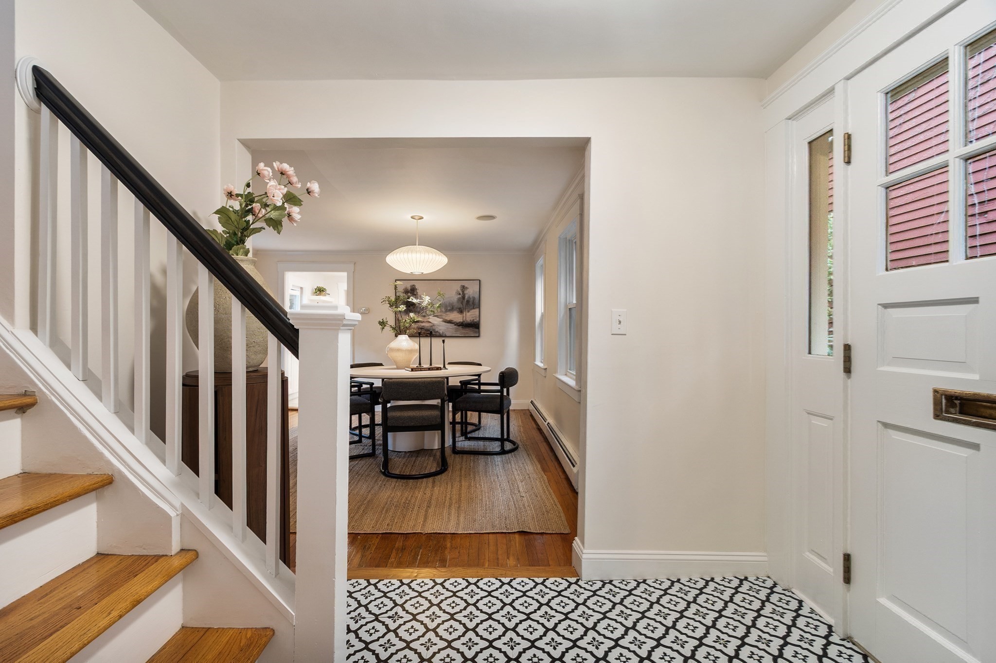 Entryway with patterned tile, wood staircase, and a dining area beyond.