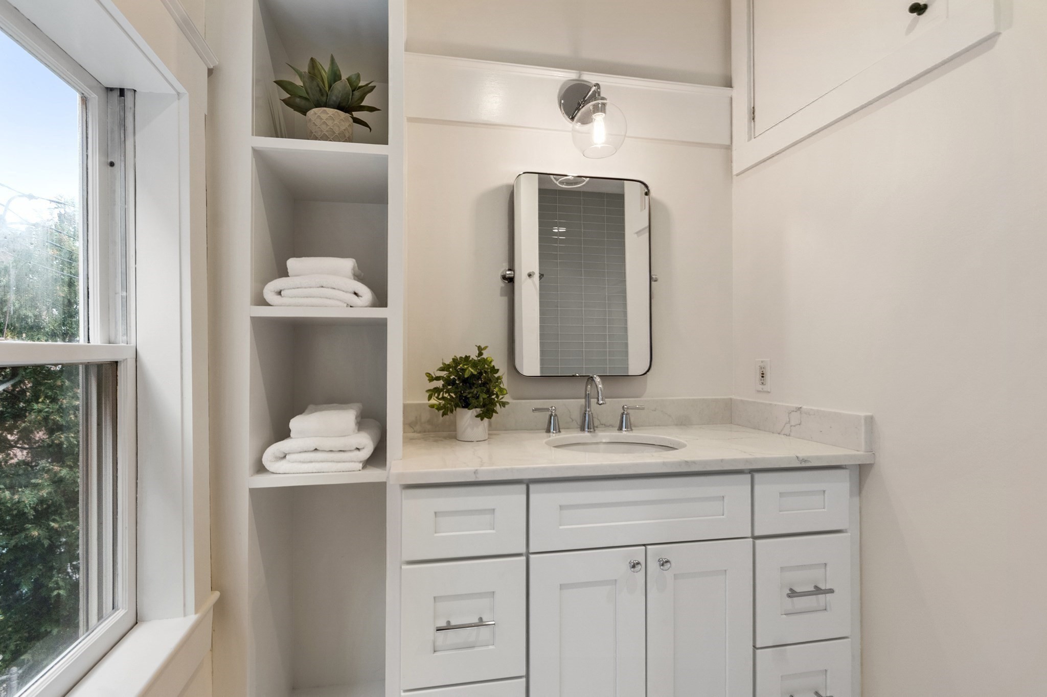 Bathroom vanity with a marble countertop, chrome fixtures, and built-in shelves of folded towels.