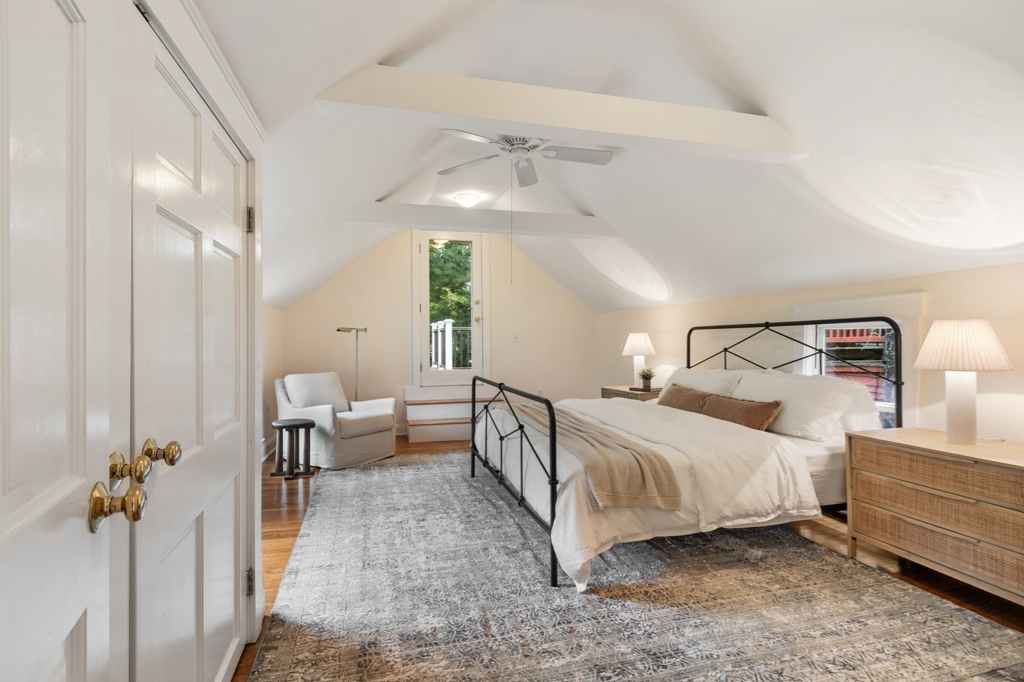 Attic bedroom with a sloped ceiling, black metal bed, and glazed door to a small balcony.