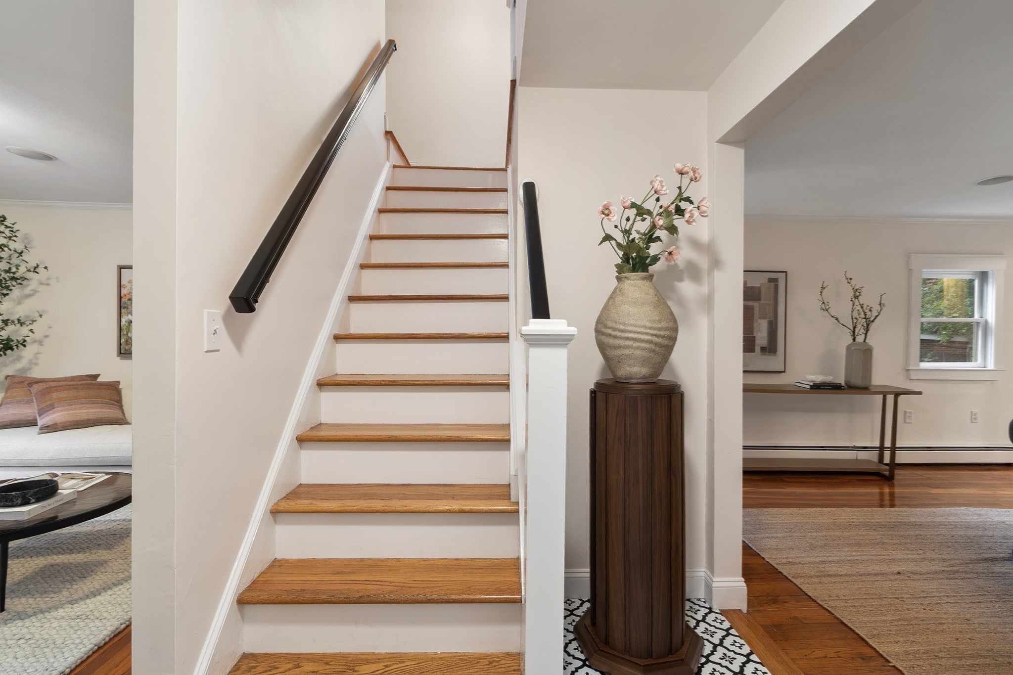 Staircase with warm wood treads and a dark handrail, flanked by furnished living spaces.