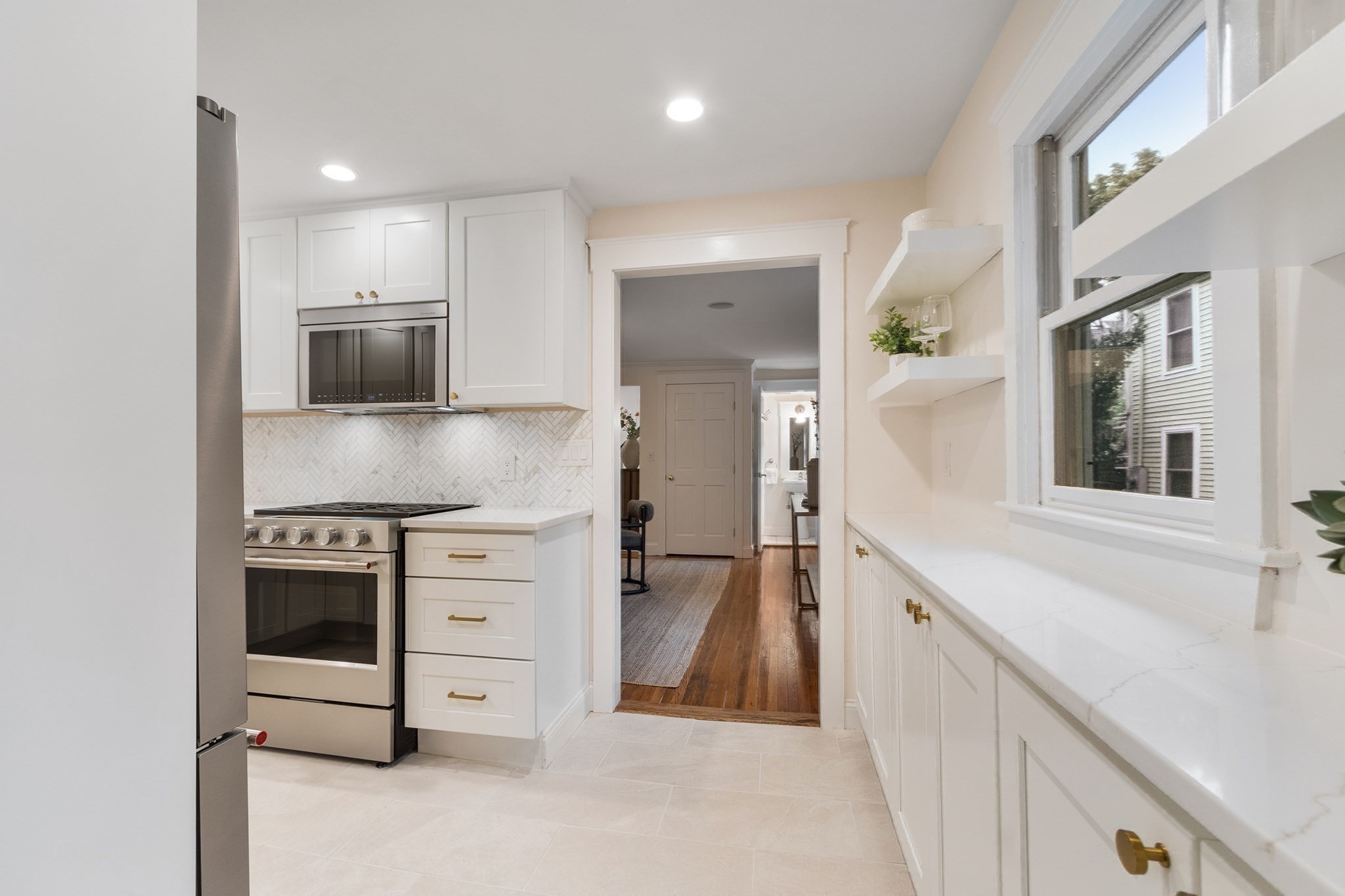 Renovated white kitchen with stainless steel range, herringbone backsplash, and long counter beneath windows.