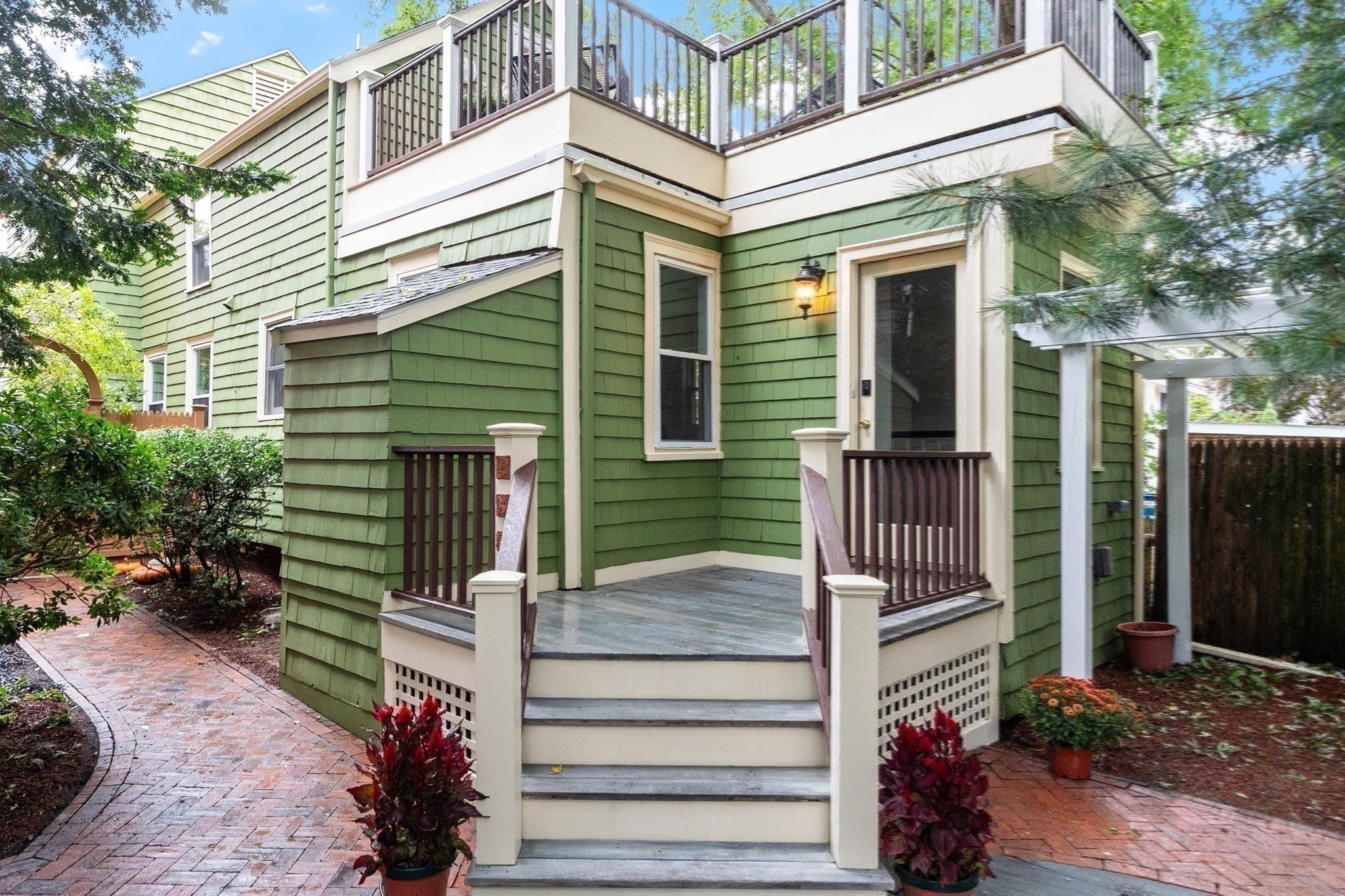 Green shingle-sided home with a raised porch, gray steps, dark railings, and an upper deck.