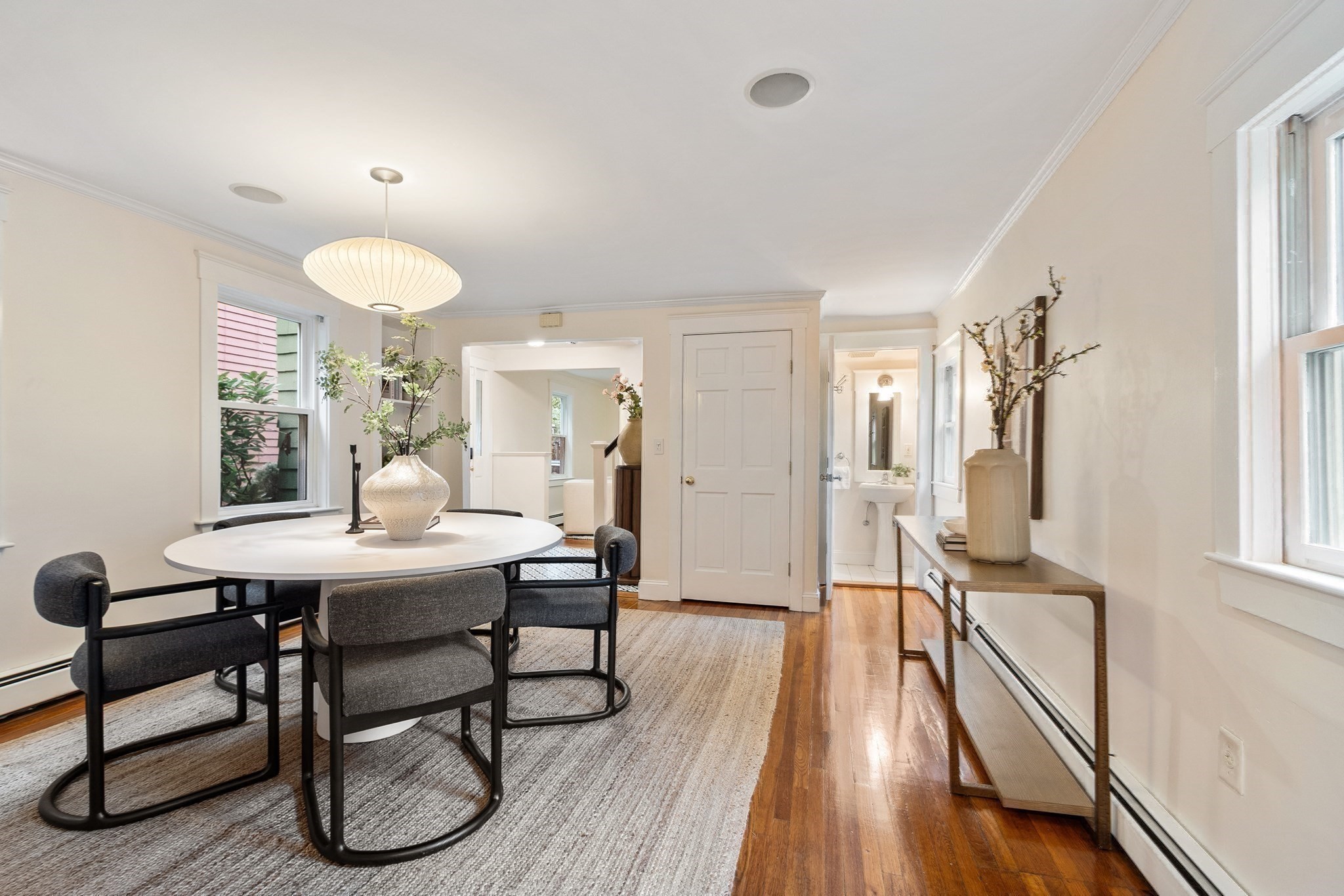 Staged dining room with a round table, gray chairs, hardwood floors, and large windows.