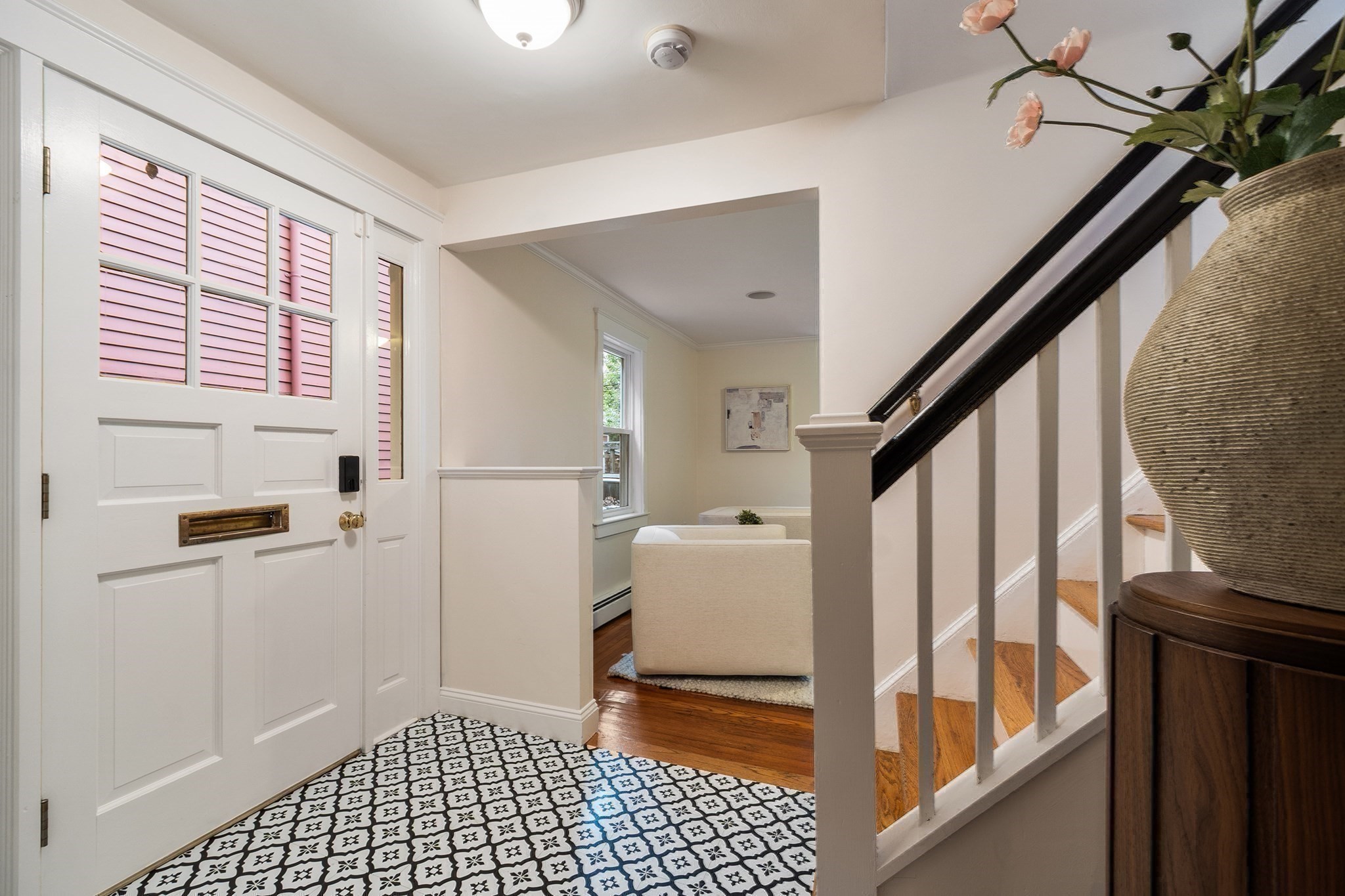 Entry foyer with patterned tile, a white paneled front door, and hardwood stairs with a dark railing.