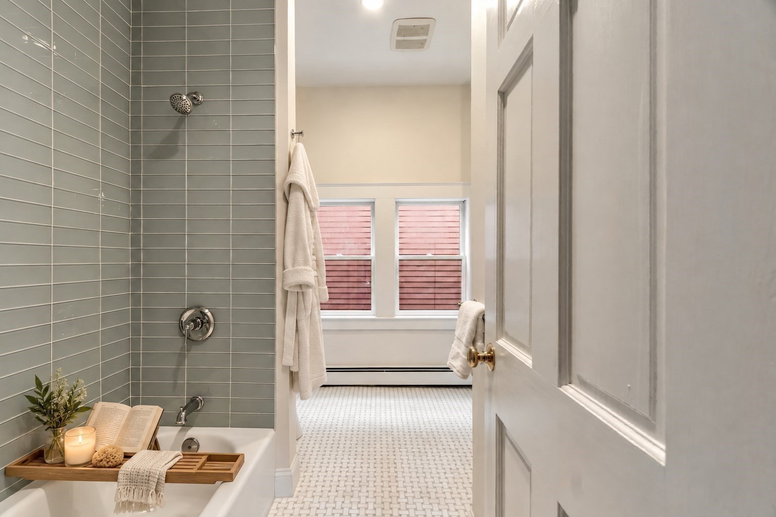 Bathroom with gray-green tiled shower, white mosaic floor, and windows with pink shutters.