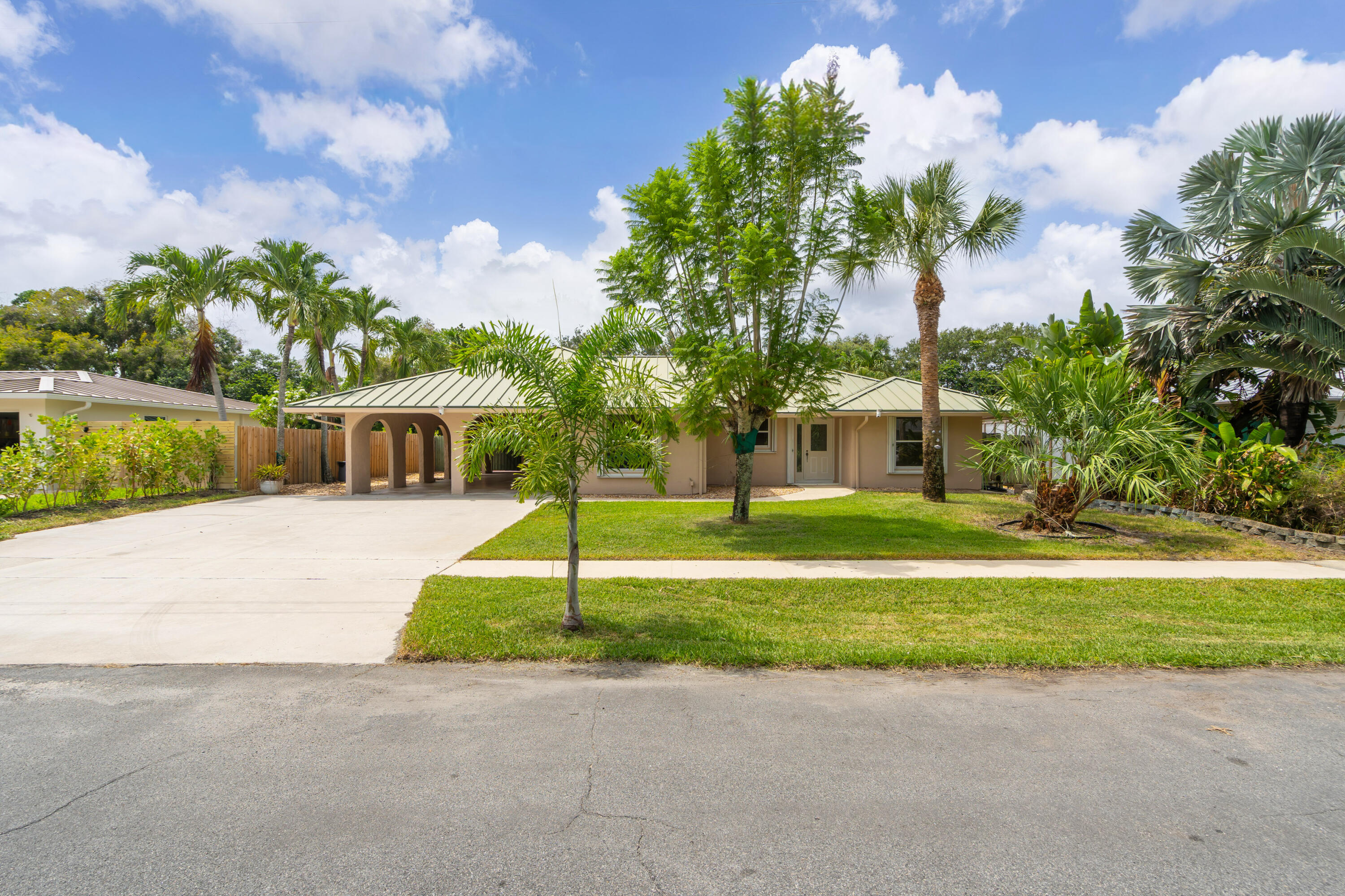 Single-story home with an arched carport, wide driveway, and tropical landscaping.