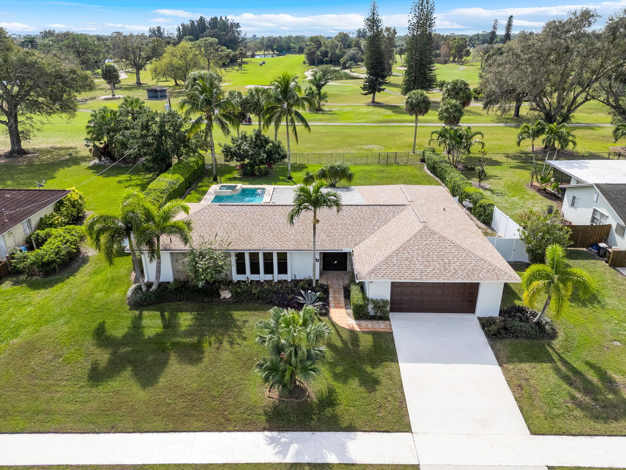 Aerial view of a white home with a pool and palm-lined lawn bordering a green golf course.