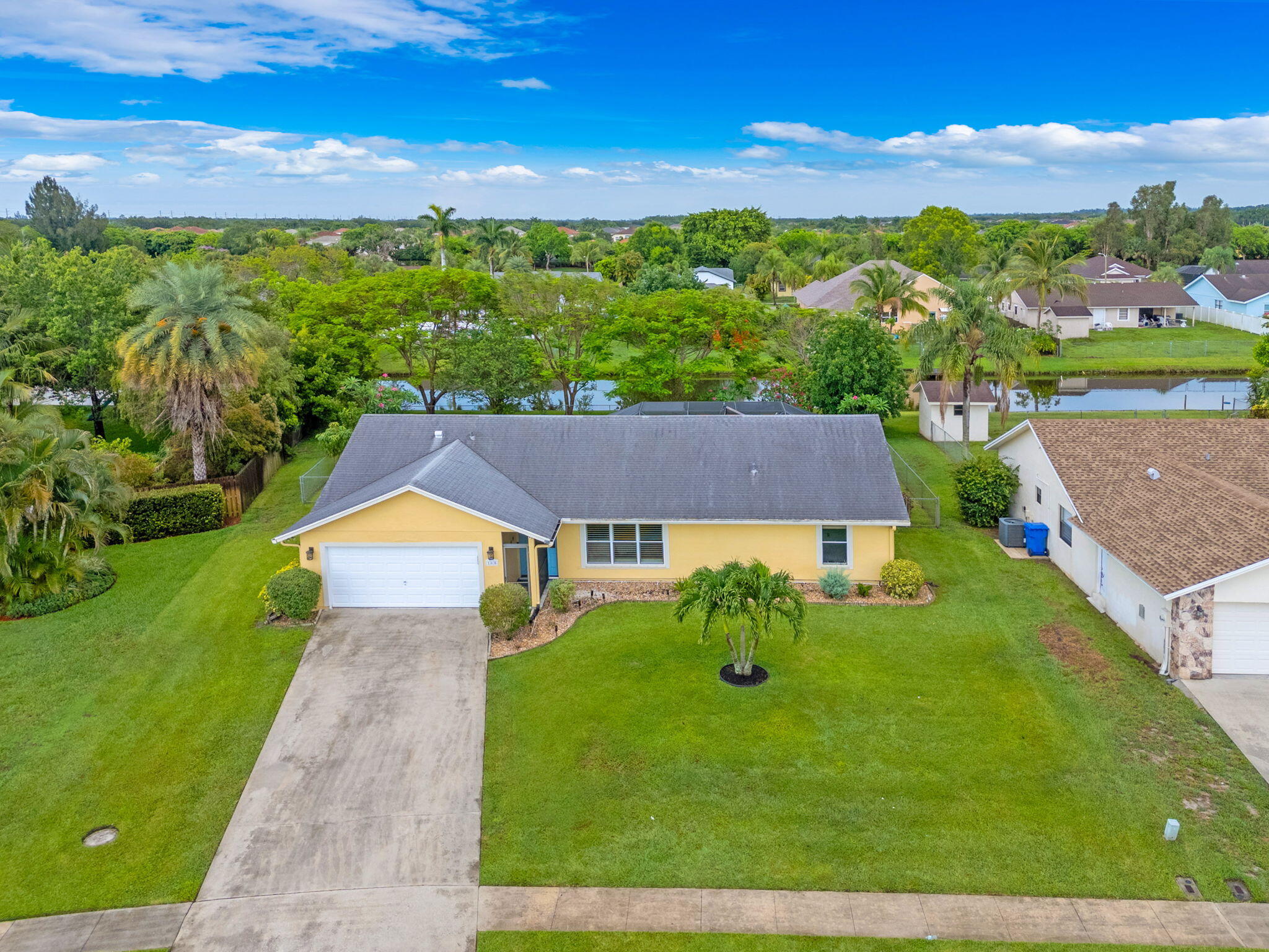 Aerial view of a yellow single-story house with a long driveway, palm trees, and a canal behind it.