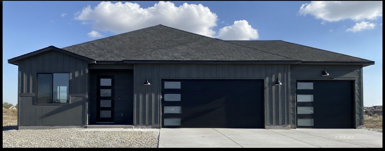 Modern dark-sided home with two garage doors, a concrete driveway, and gravel landscaping.