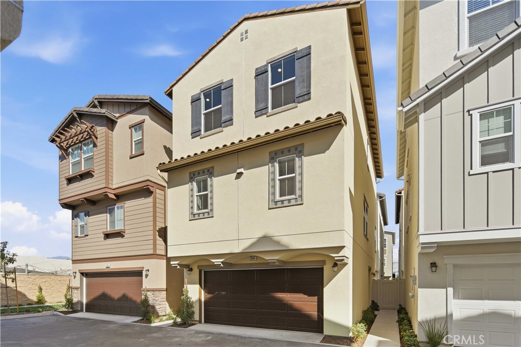 Cream stucco townhouse with dark shutters and a double garage, between two neighboring homes.