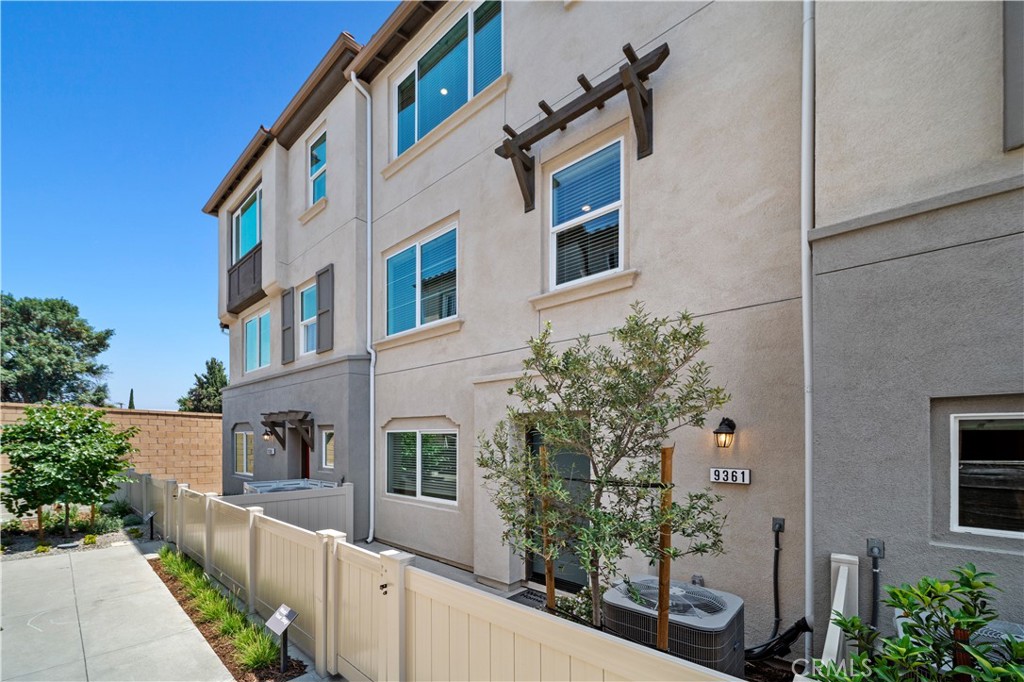 Multi-story stucco home with a fenced walkway and young trees along the exterior.