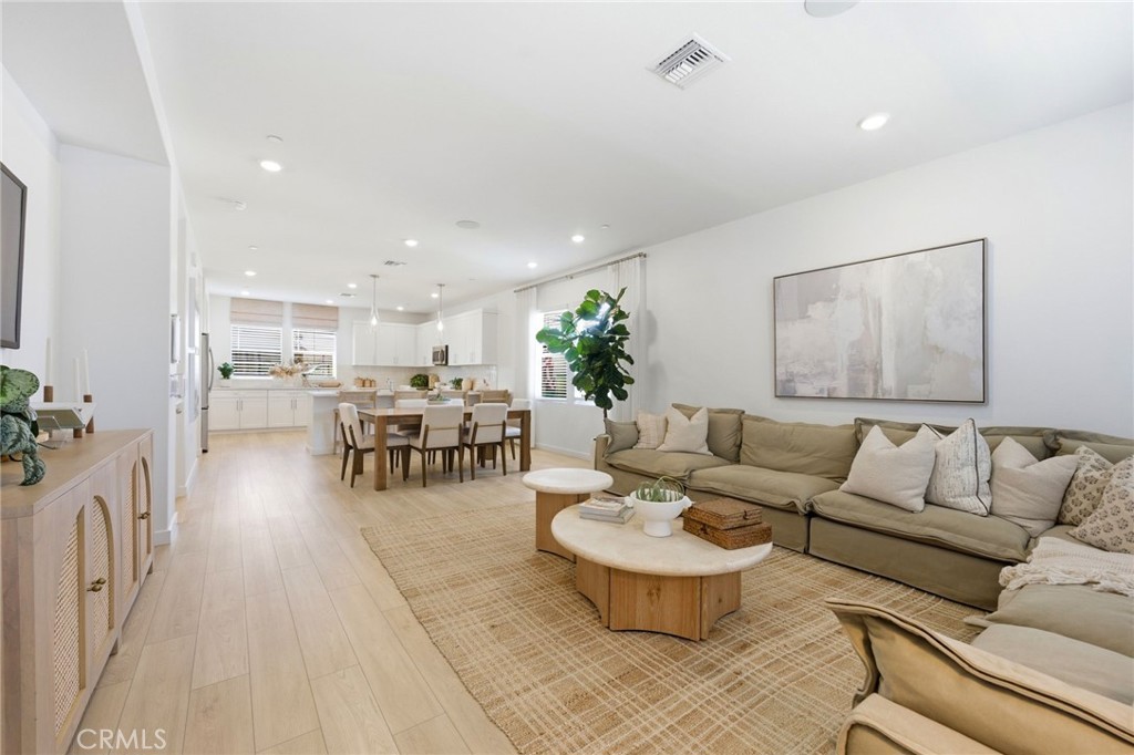 Open-plan living room with a beige sectional, round wood coffee tables, and an adjacent dining area.