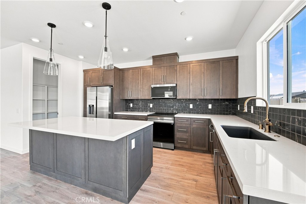 Modern kitchen with a large island, dark cabinetry, black tile backsplash, and a farmhouse sink.