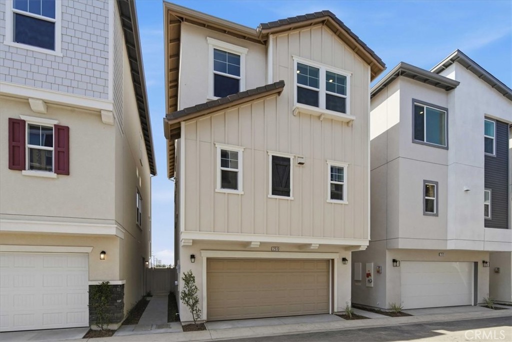 Three-story beige townhouse with a two-car garage between neighboring homes.
