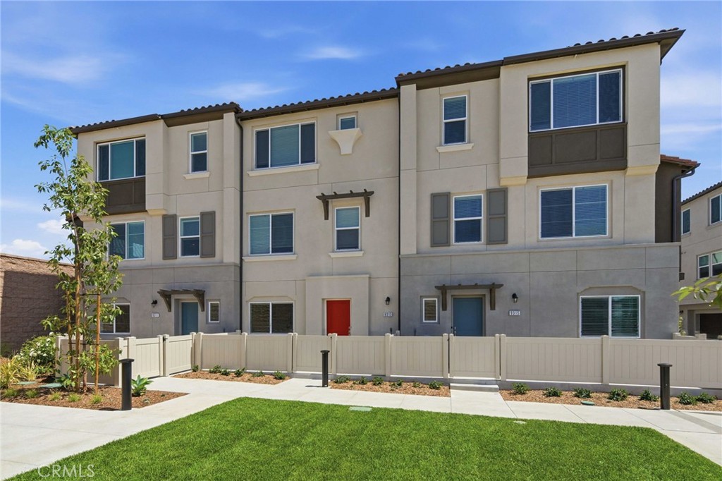 Three-story attached townhomes with fenced patios and a green lawn.