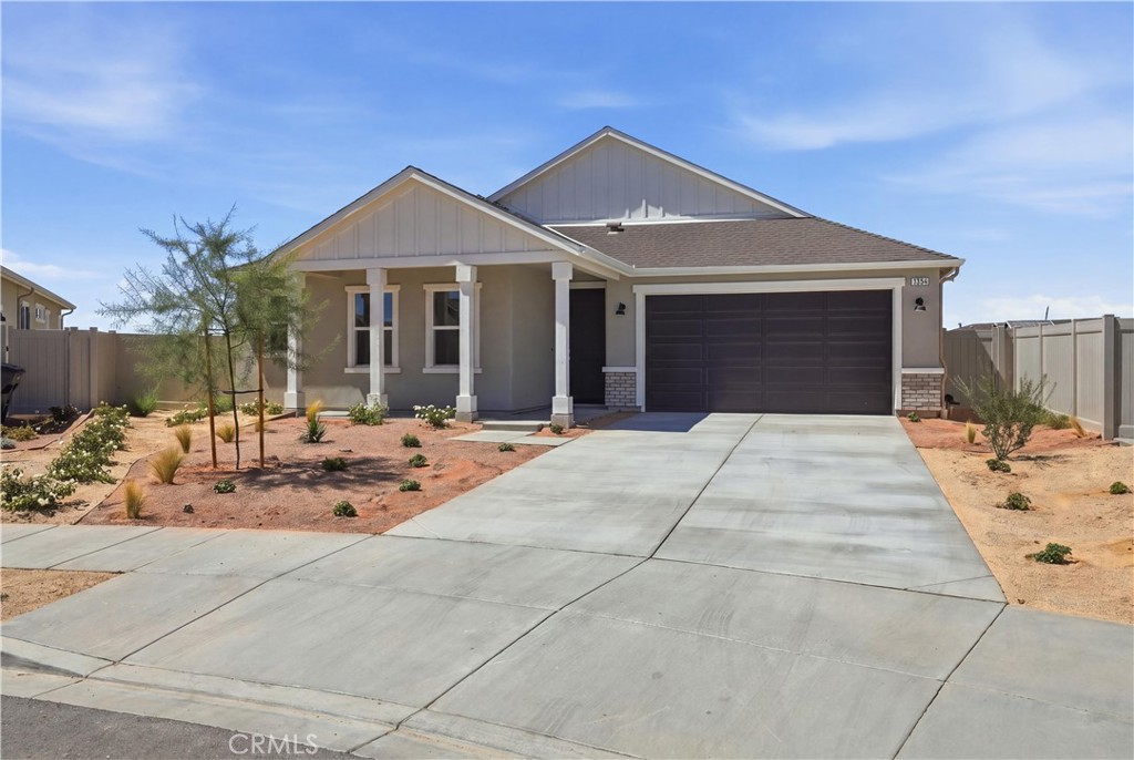 Single-story gray home with a covered porch, double garage, wide driveway, and desert landscaping.