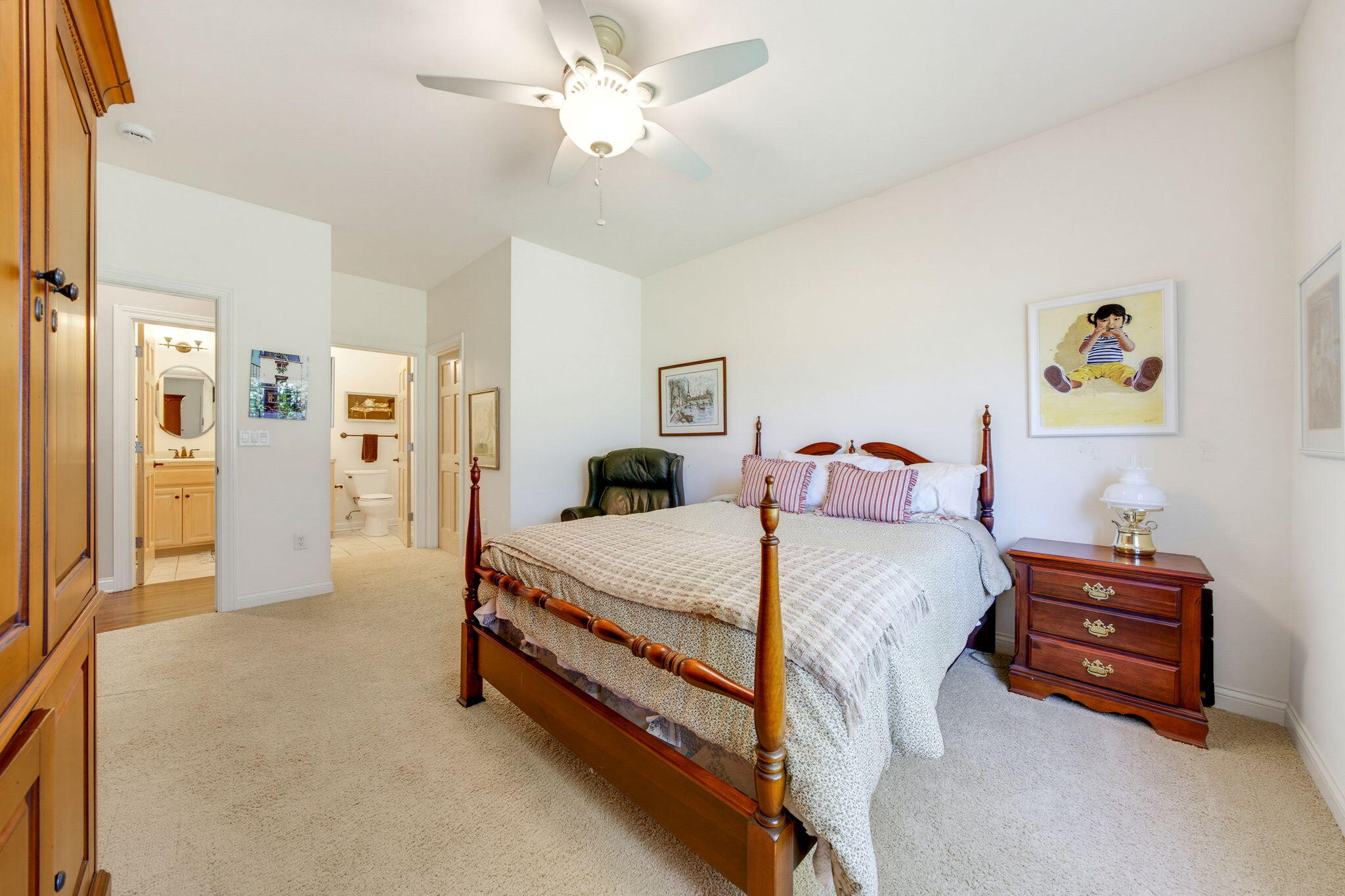 Bedroom with a wooden four-poster bed, cream bedding, ceiling fan, and adjoining bathroom doorways.