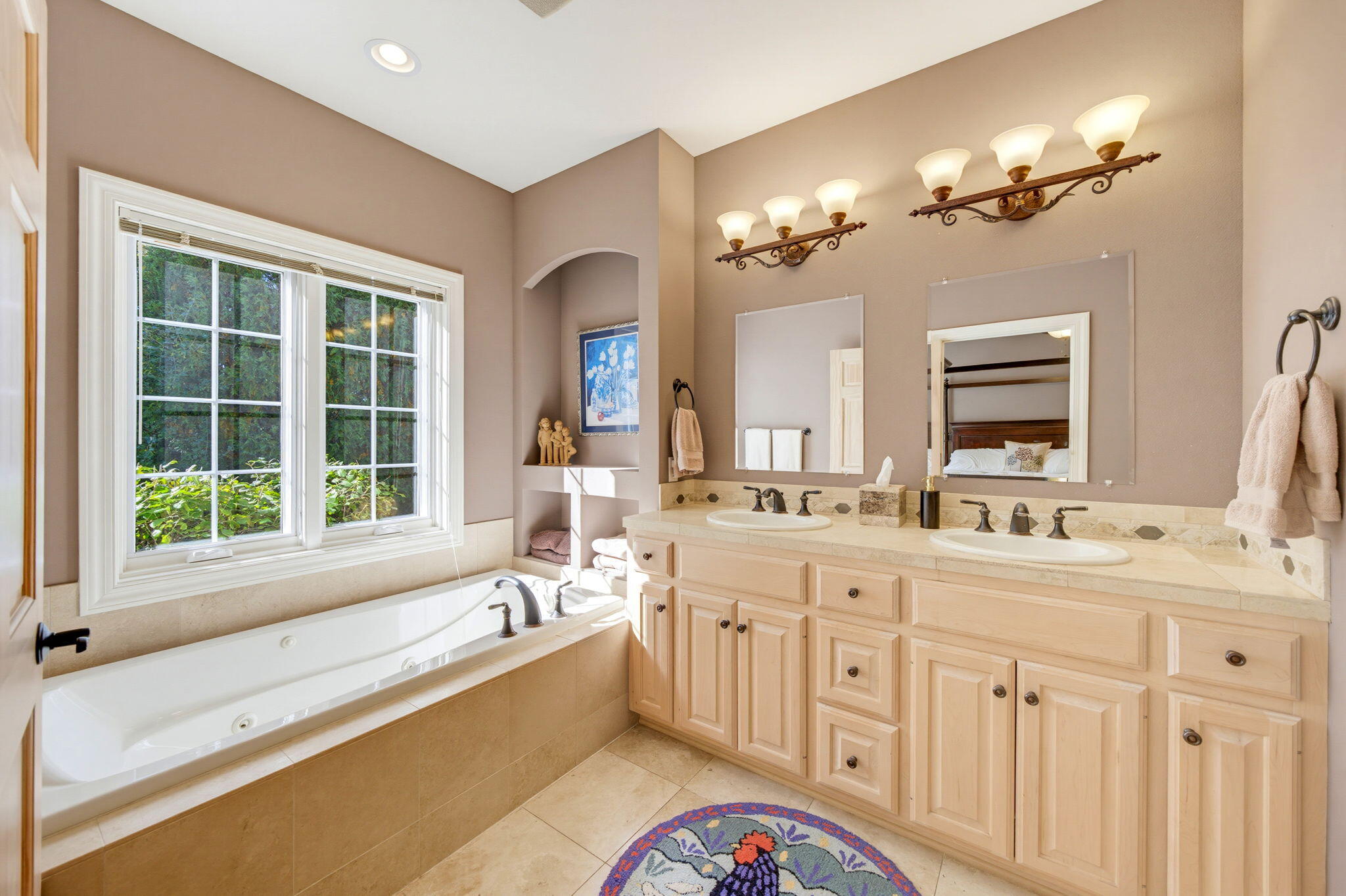 Primary bathroom with a soaking tub beneath a large window and a long double-sink vanity.