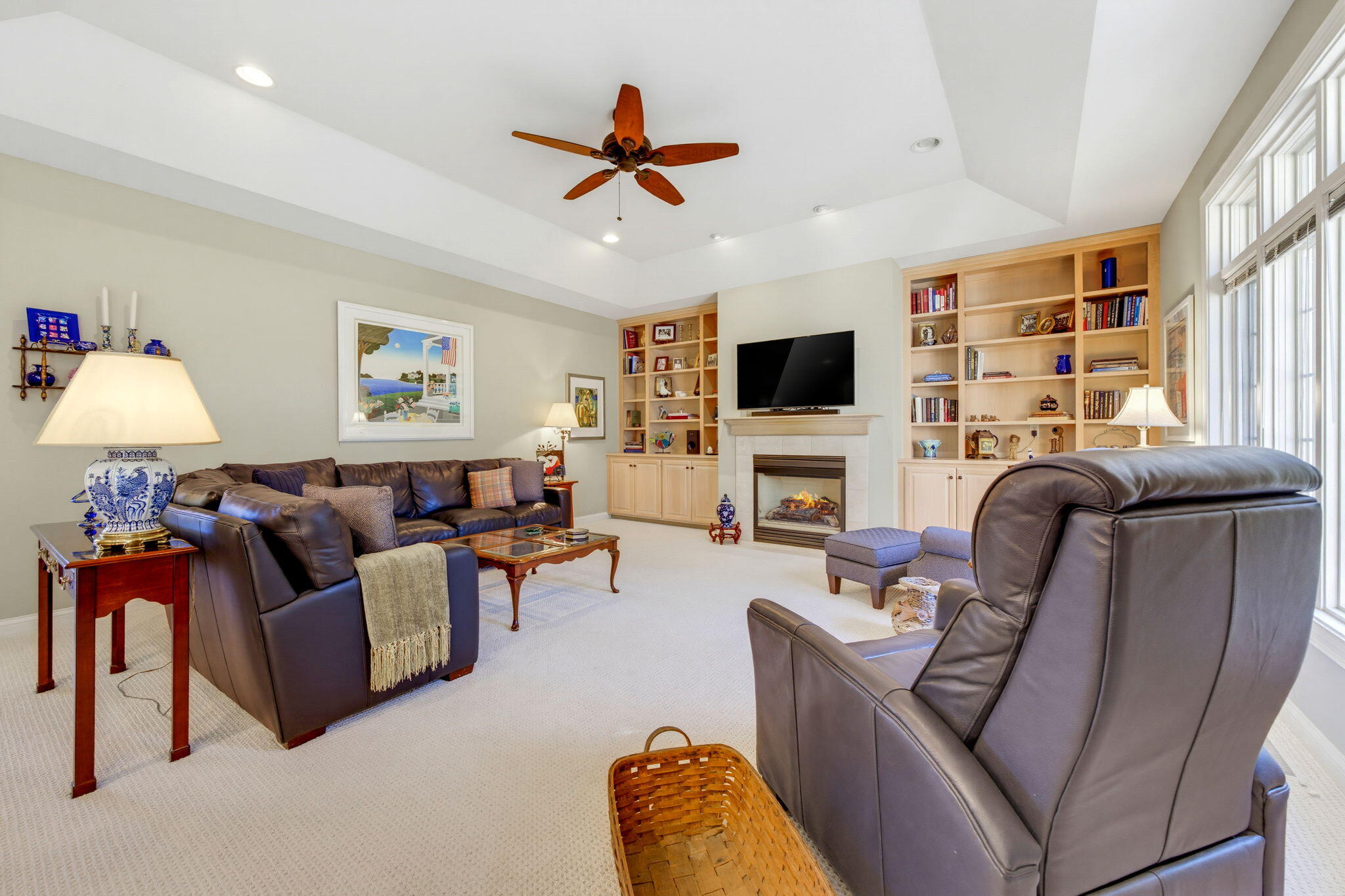 Furnished living room with leather seating, a fireplace, built-in bookcases, and large windows.