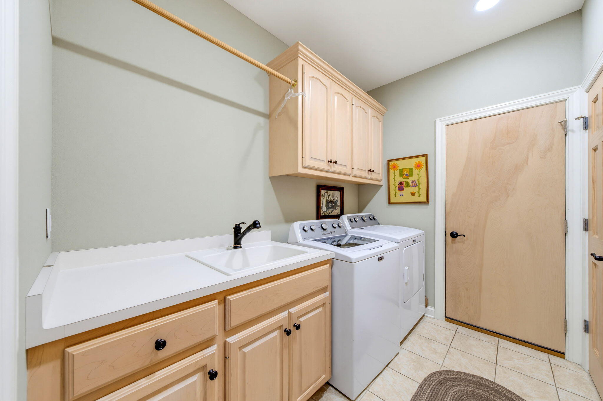 Laundry room with washer and dryer, utility sink, and light wood cabinetry.