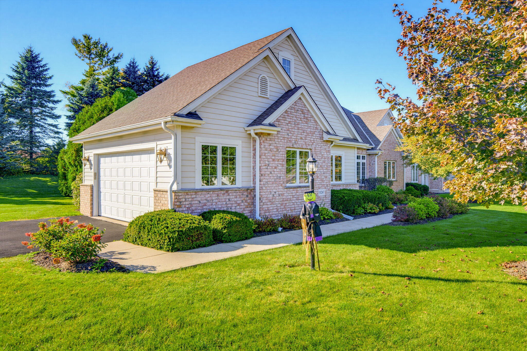 Home exterior with brick accents, attached garage, landscaped lawn, and a Halloween scarecrow by the walkway.
