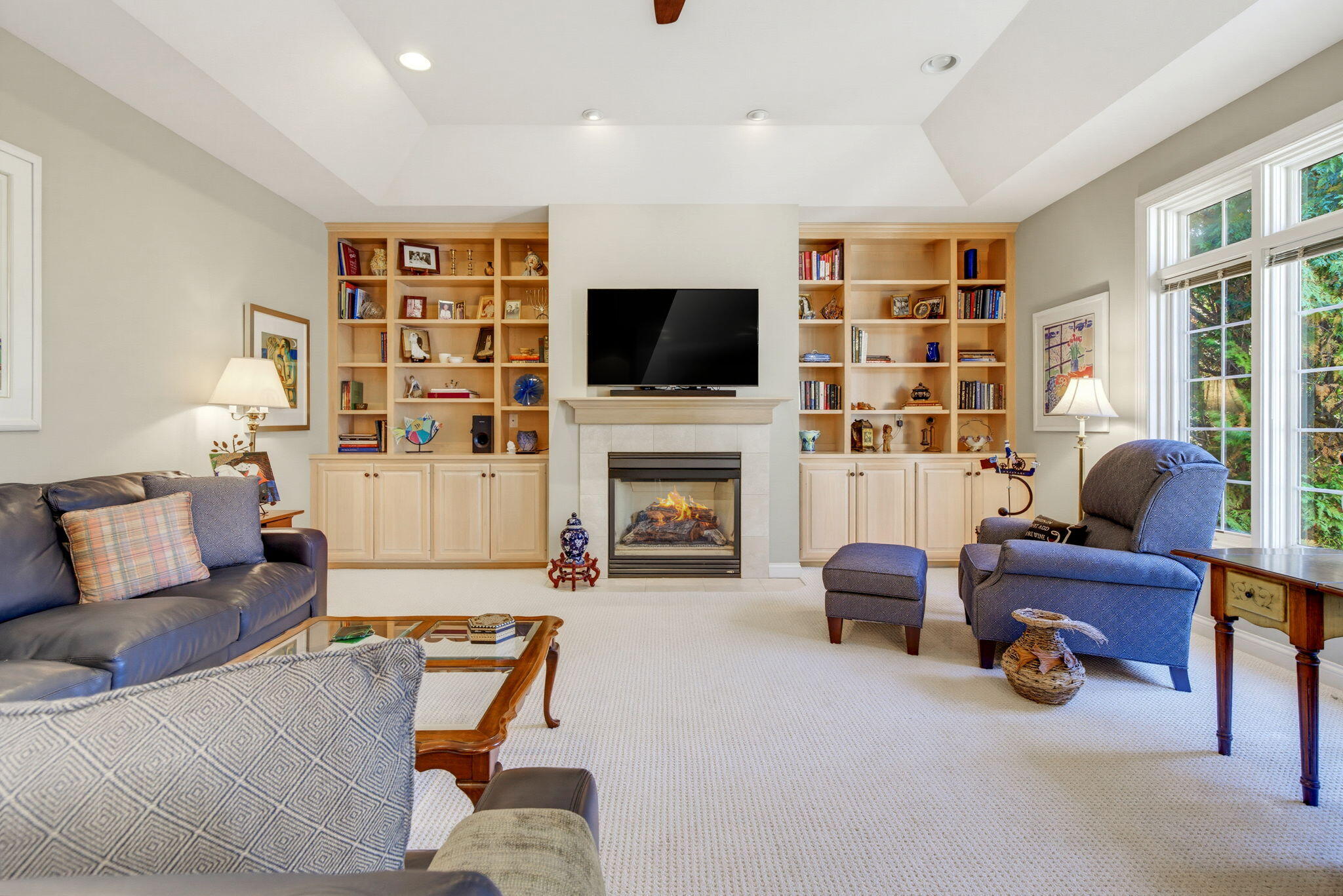 Living room with built-in bookshelves, a fireplace, and blue seating beside large windows.